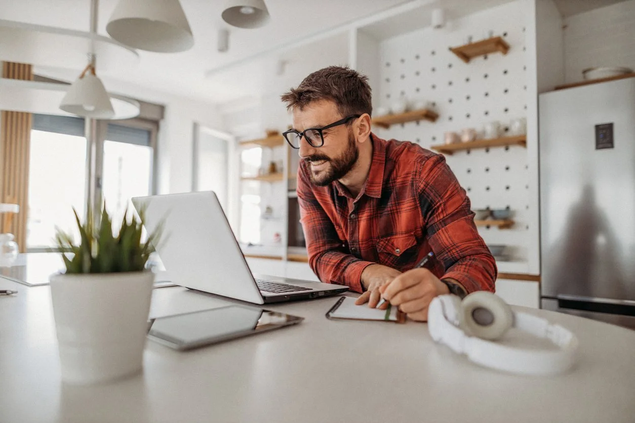 Man on laptop in kitchen working with an executive function coach on remote executive function coaching in Colorado