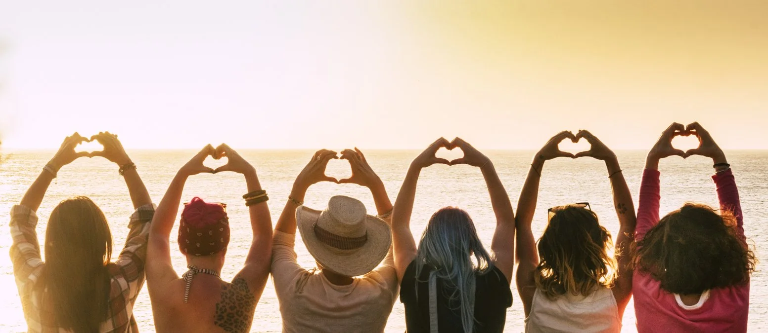 Group of empty nest women standing on the beach at sunset, making heart shapes with their hands, executive function courses concept