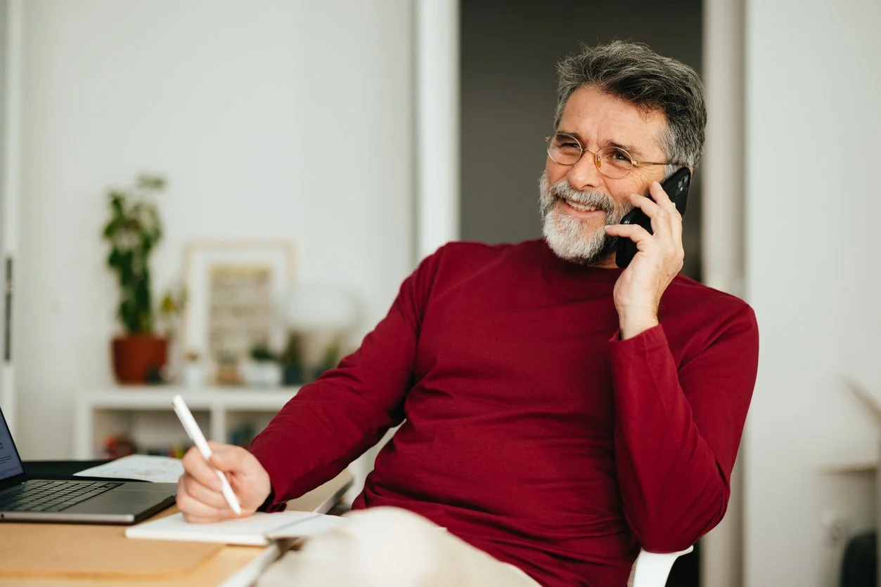 Mature coach on the phone with an executive function coach for coaches smiling while taking notes