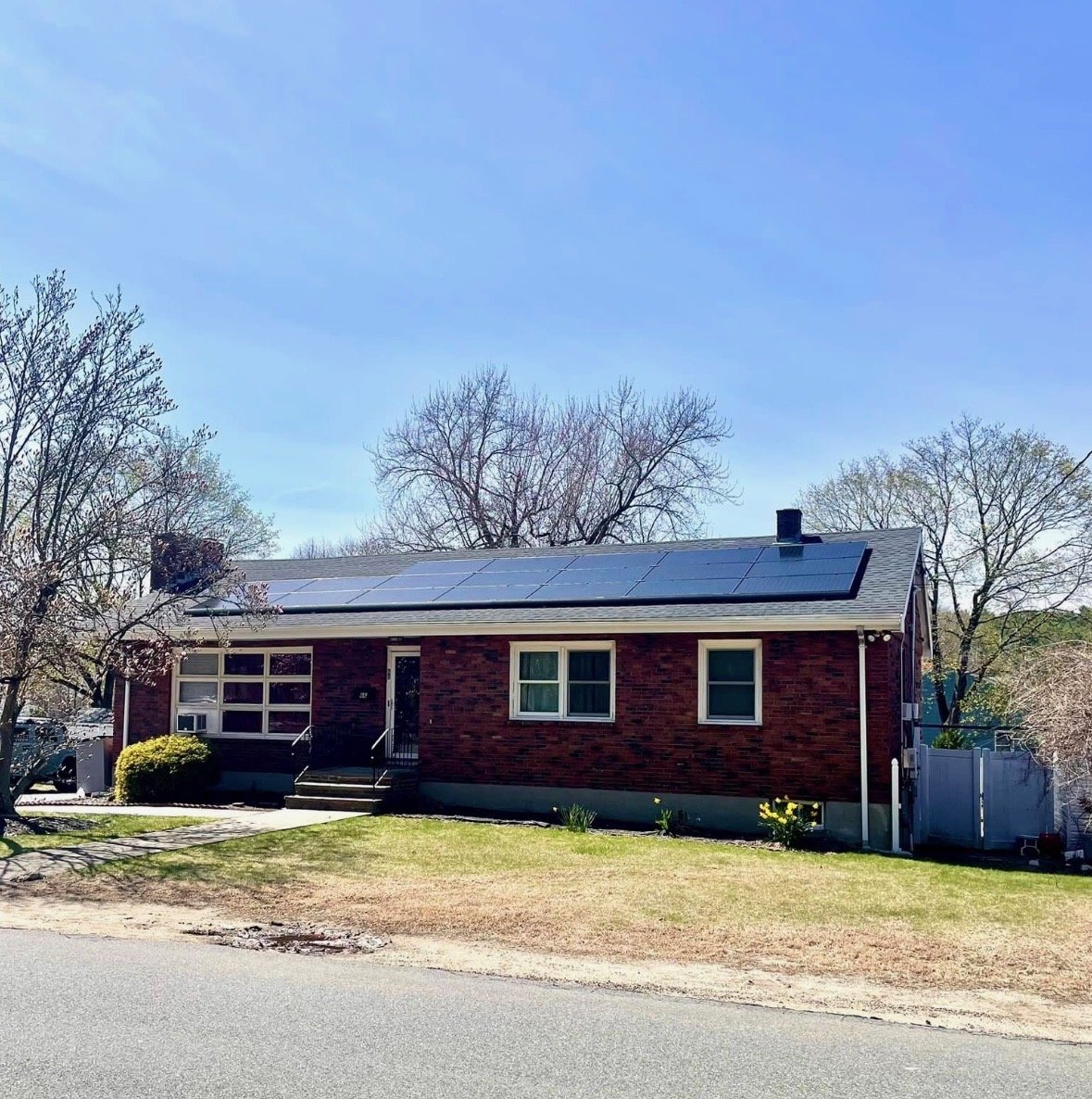 A brick house with solar panels on the roof, trees in the background, and a lawn in front.