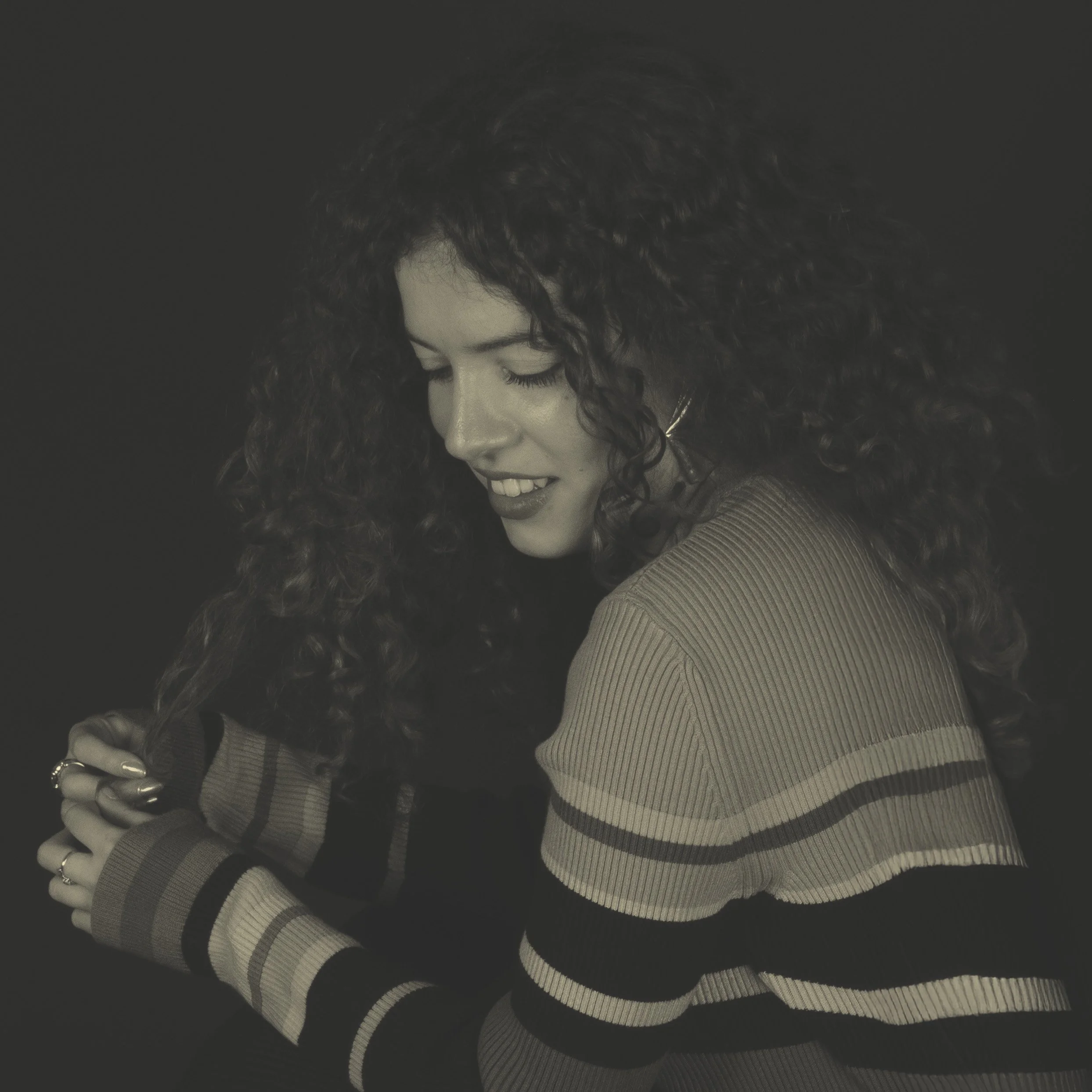 Une jeune femme aux cheveux bouclés utilisant un peigne et souriant, avec un fond sombre.
