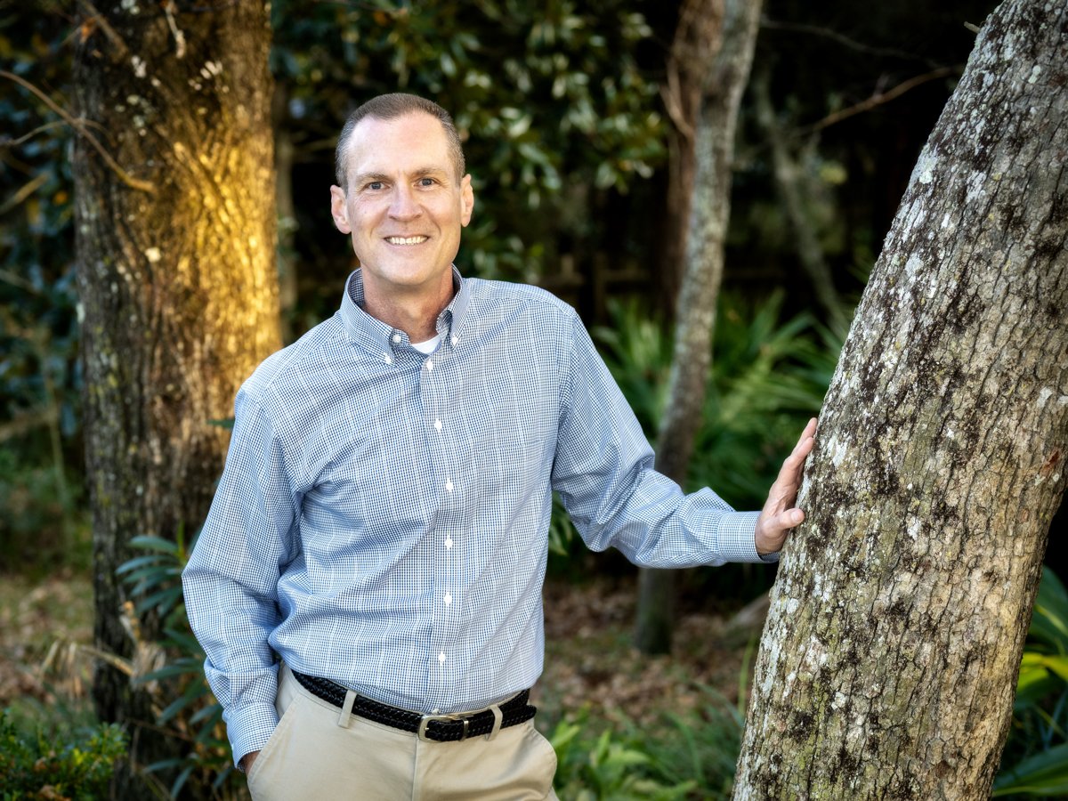 David Roberts, fiduciary planner for veteran business owners, smiling outdoors among trees in a light blue button-down shirt.