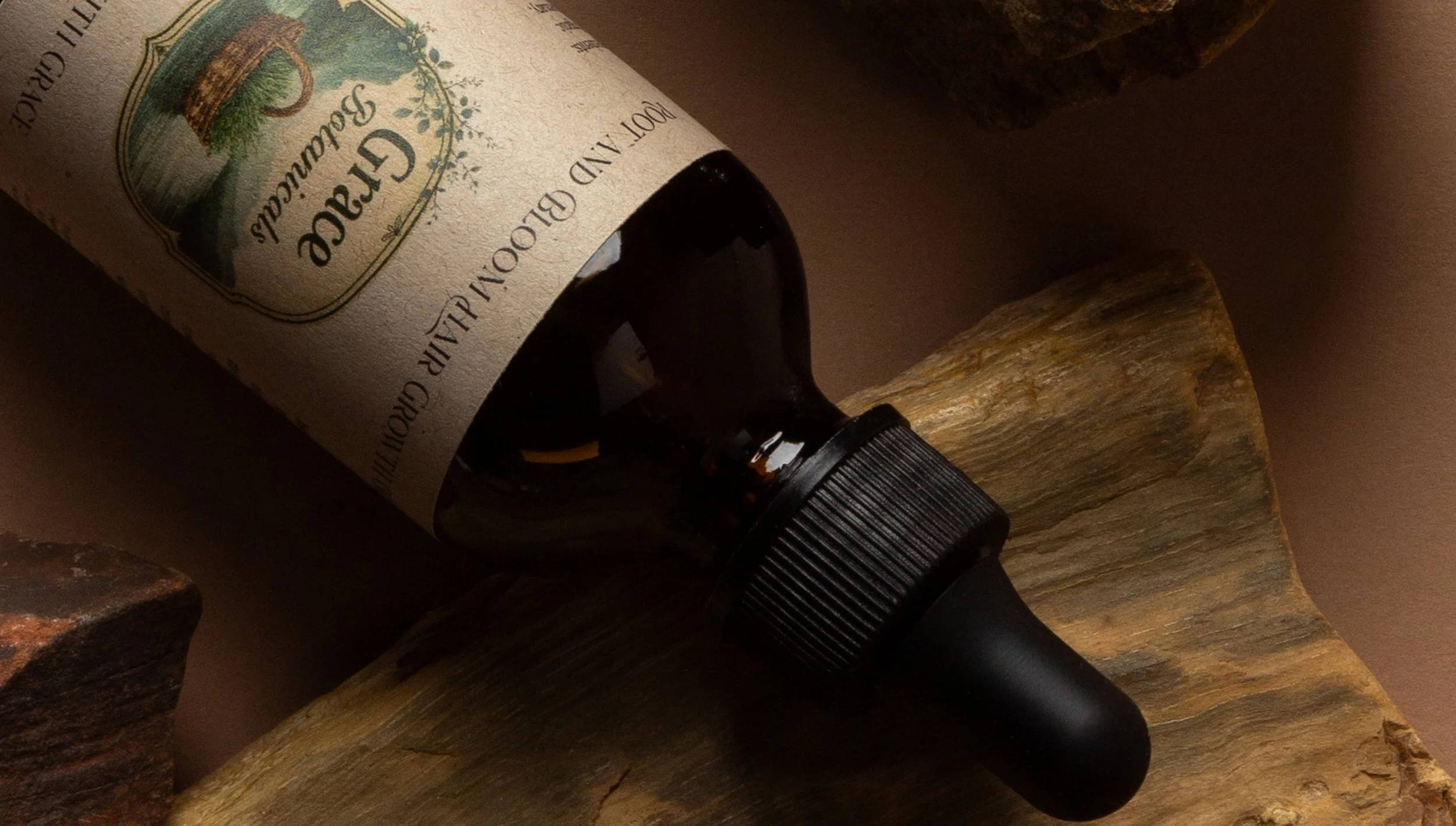 A dark amber bottle lying on a piece of wood with a dropper attachment, partially showing a label with green and yellow design elements.