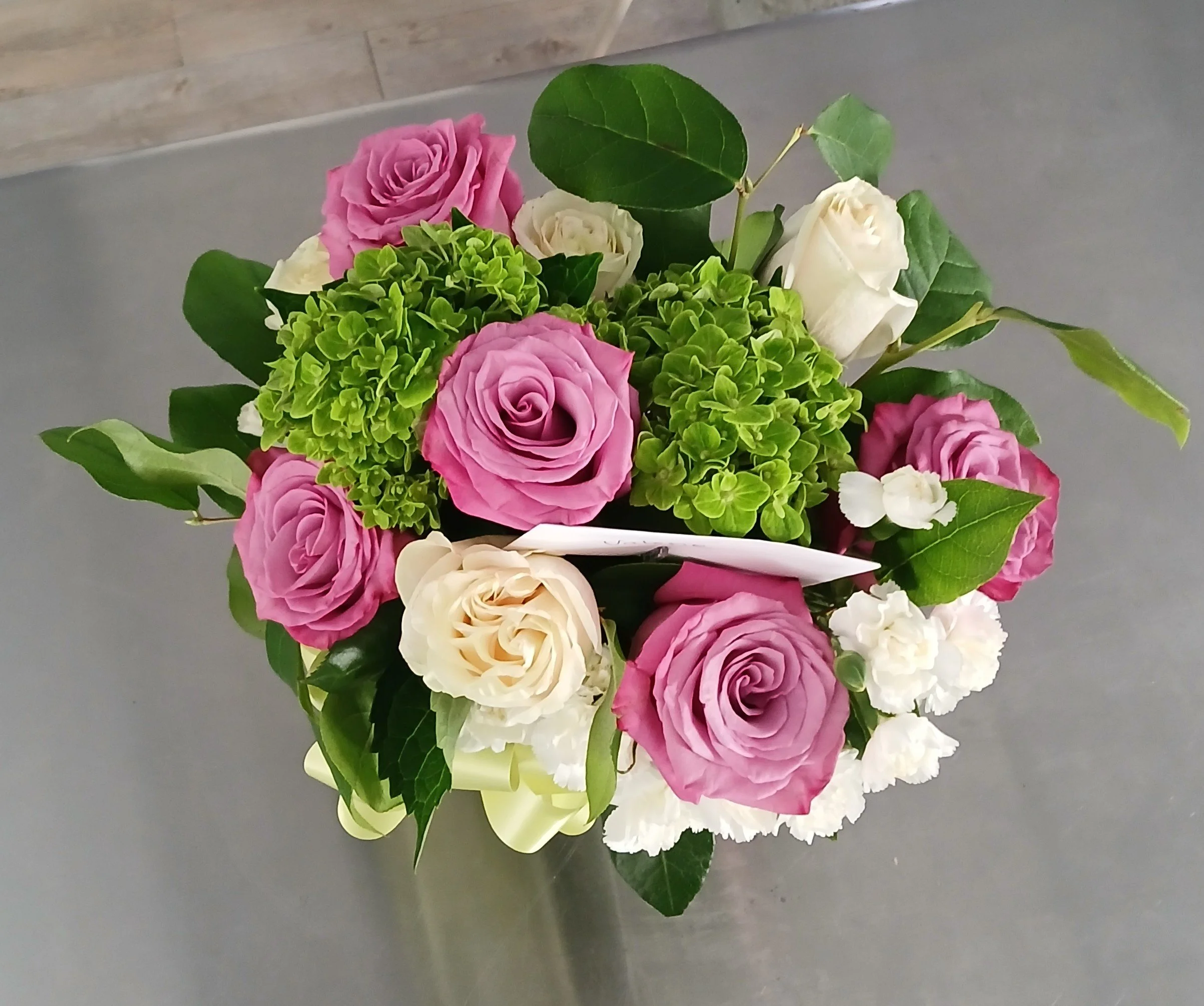 A bouquet of pink, white, and green flowers including roses, hydrangeas, and other blossoms arranged with green leaves.
