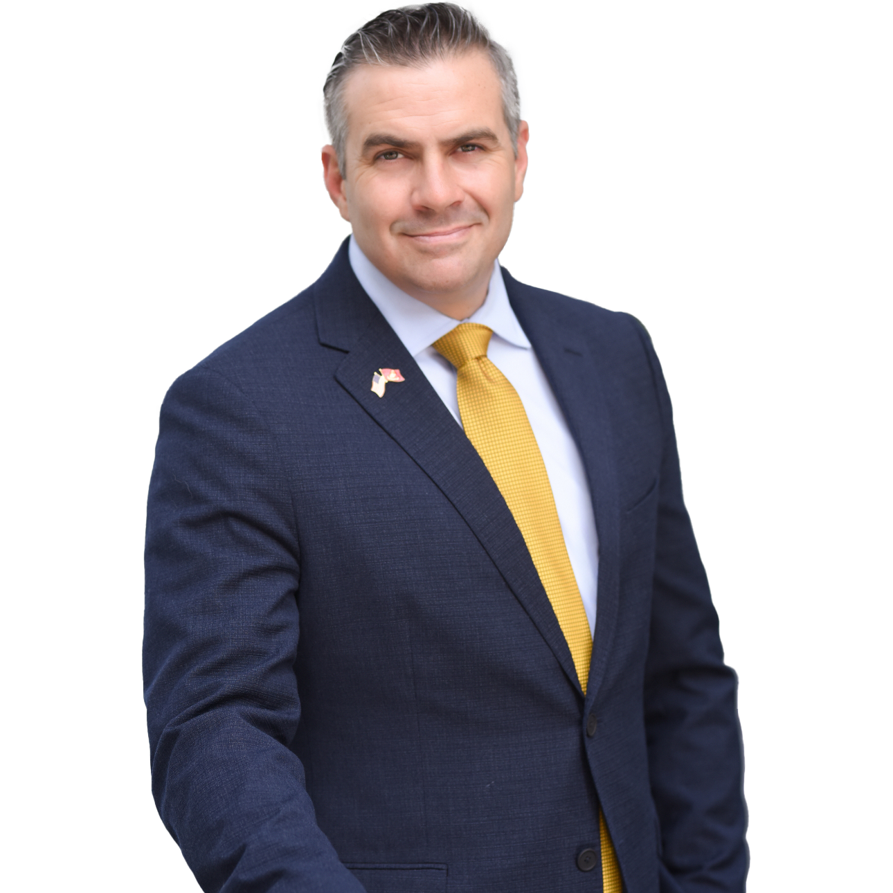 David Serpa in a navy blue suit with a gold tie, wearing an American flag lapel pin, smiling at the camera.