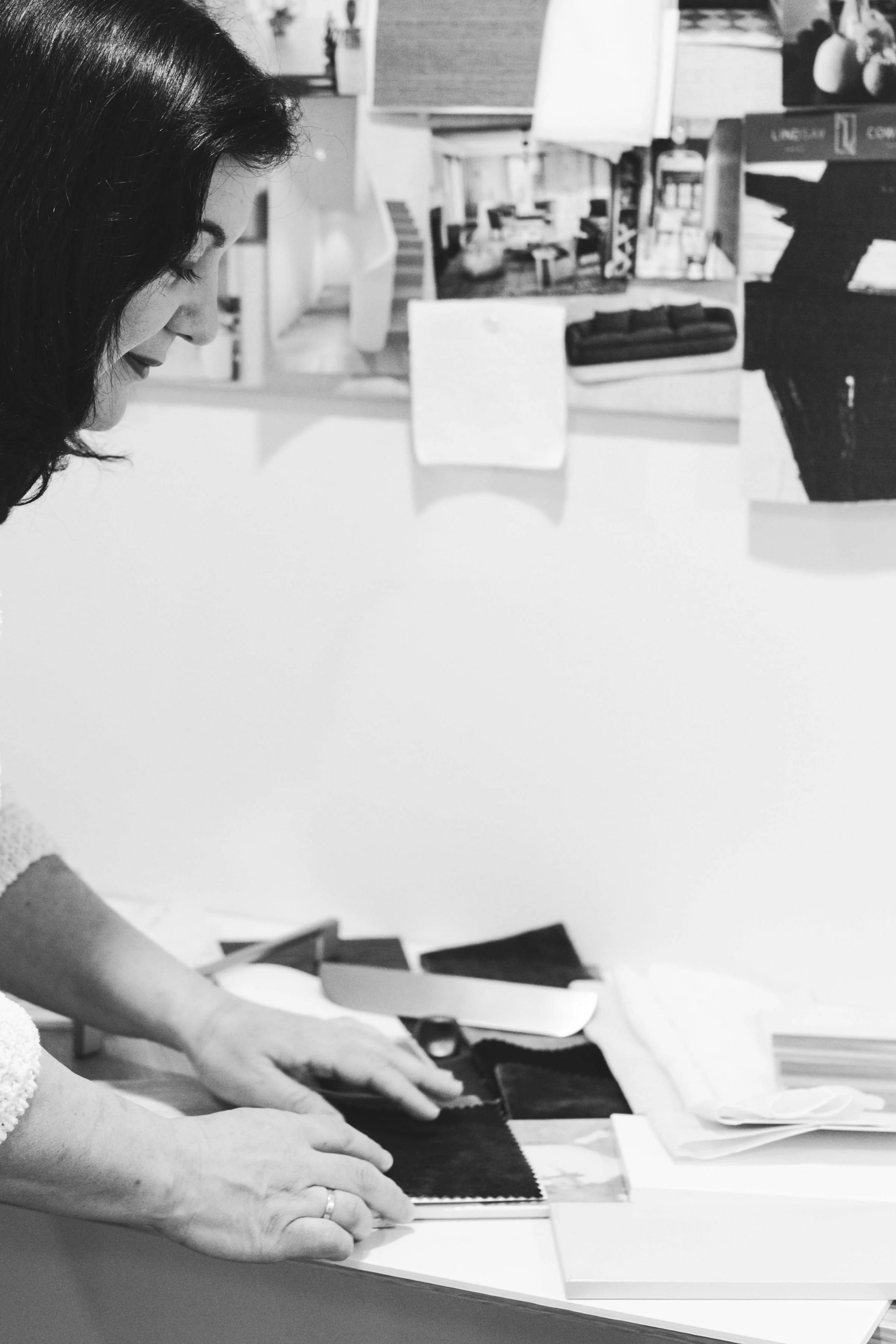 A woman with dark hair looking down at fabric swatches on a table, in a room with artworks and shelves in the background.