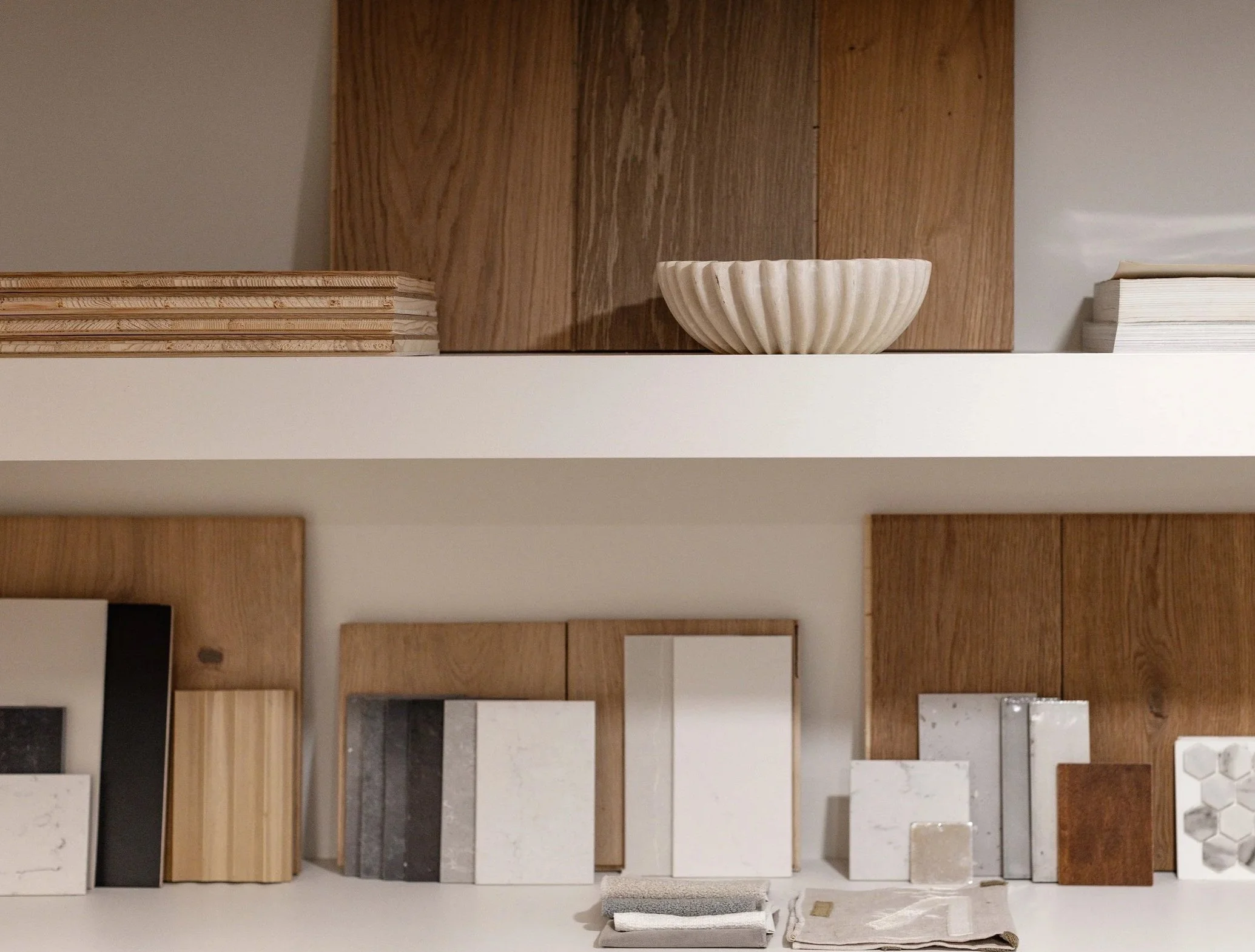 Display of various tile samples and color swatches arranged on white shelves, with wooden panels in the background.