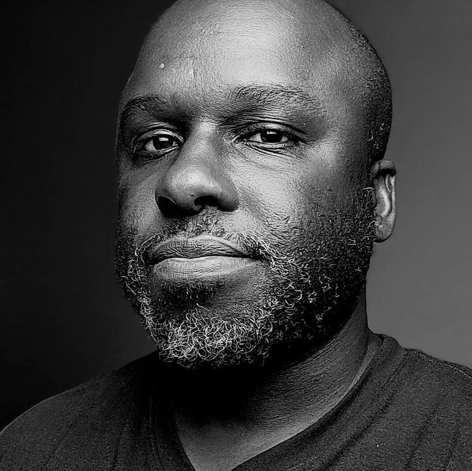 Multidisciplinary Artist Mario DeBlak Robinson looks forward in a black and white profile shot with high contrasting light