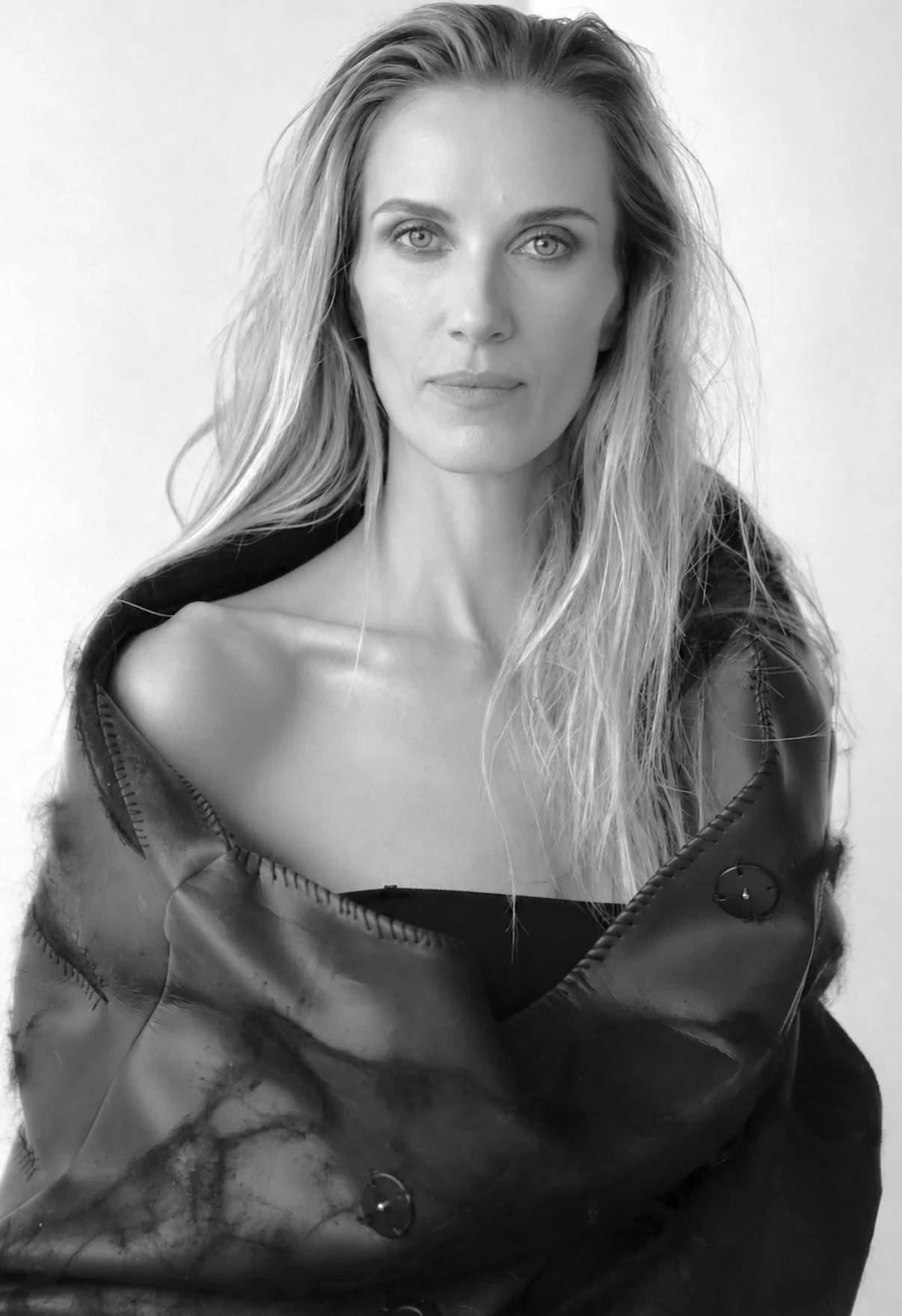 Black-and-white portrait of a woman with long, wavy hair, wearing a slightly open jacket, looking directly at the camera with a neutral expression.