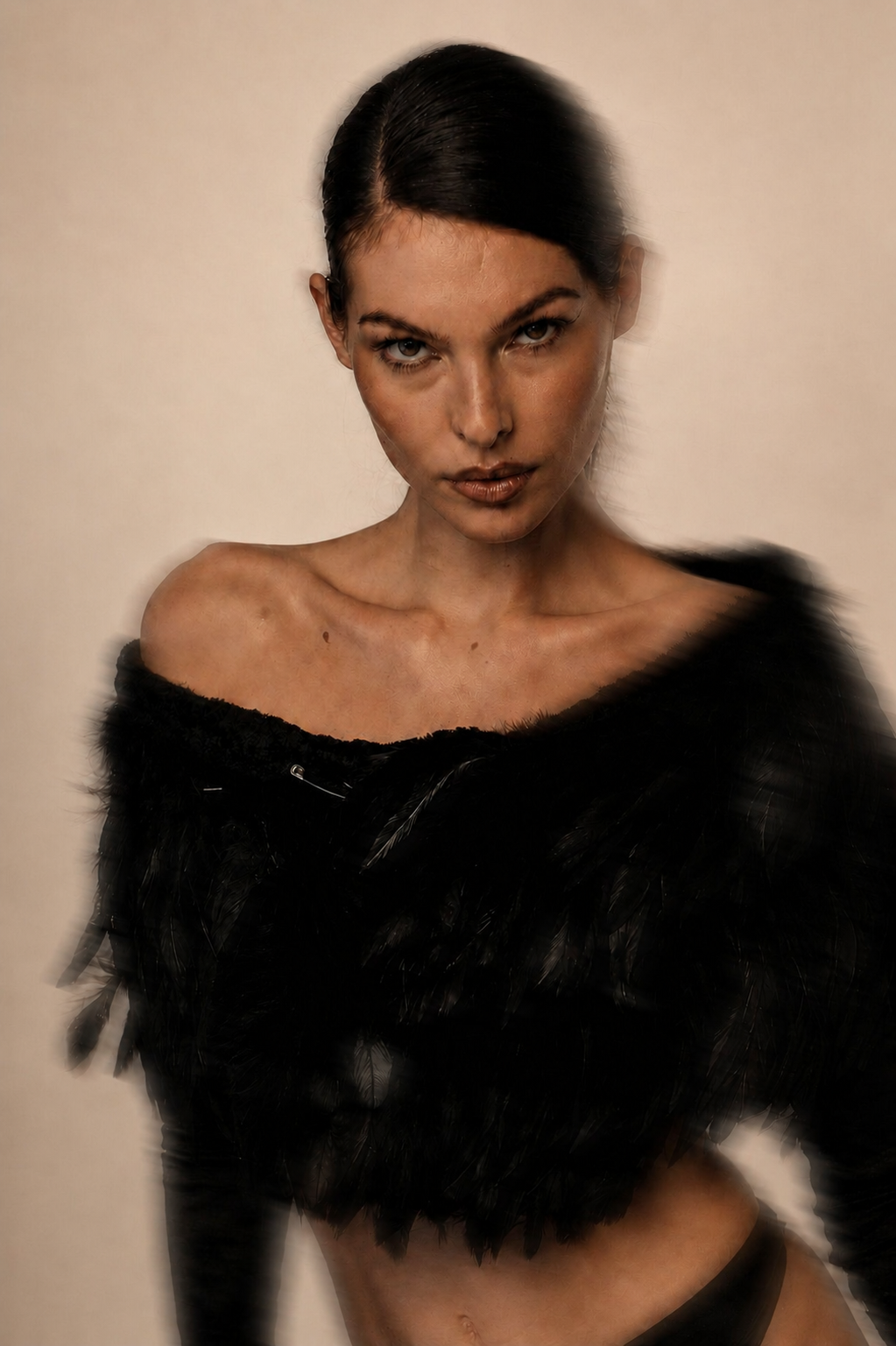 A young woman with dark hair, wearing a black feathered off-shoulder top, looking directly at the camera with an intense expression, against a plain light background.
