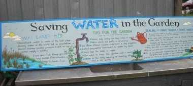 Educational sign about saving water in the garden with illustrations of a faucet, watering can, and plants.