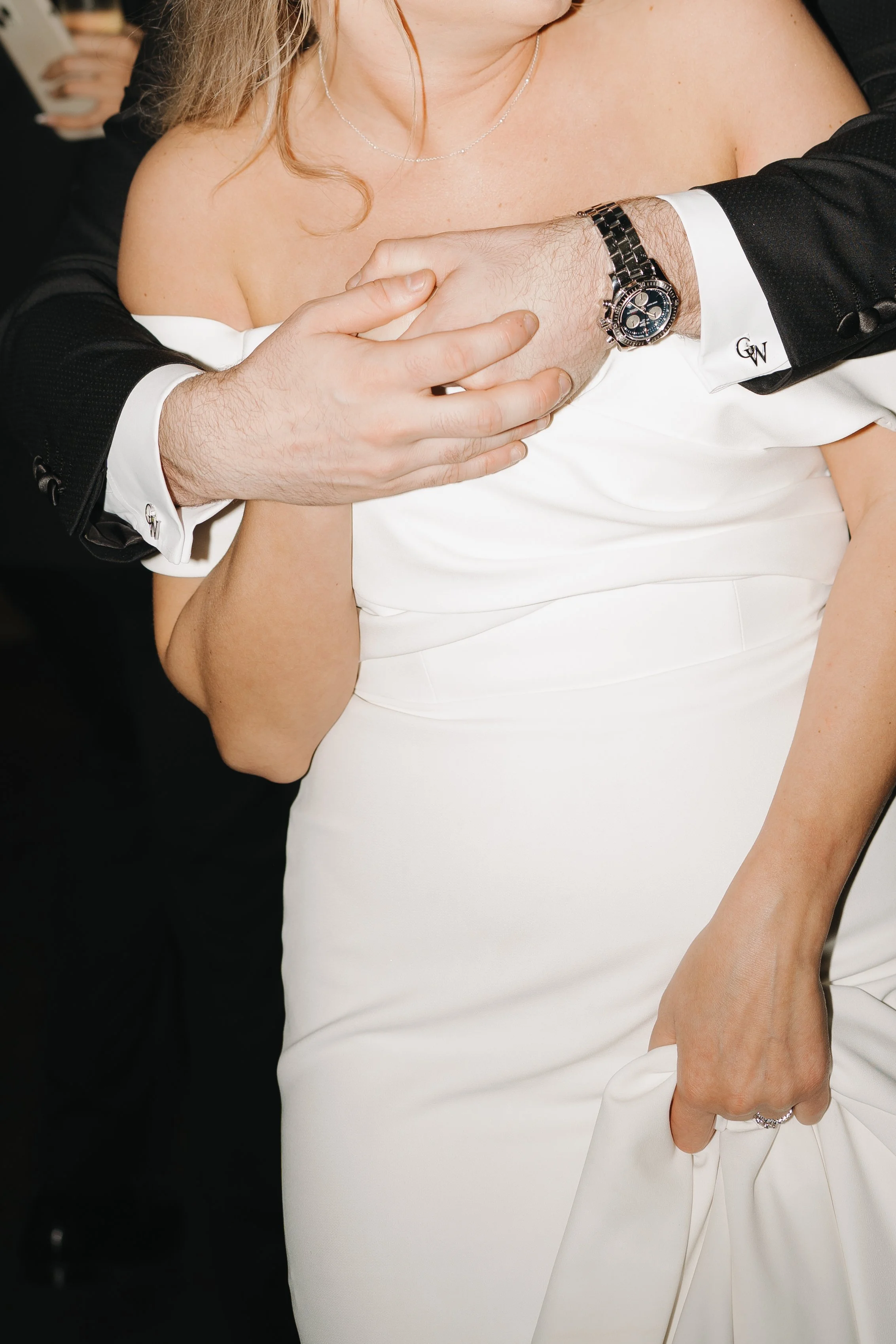 Close-up of a person in a white dress holding hands with another person in a tuxedo at a formal event.