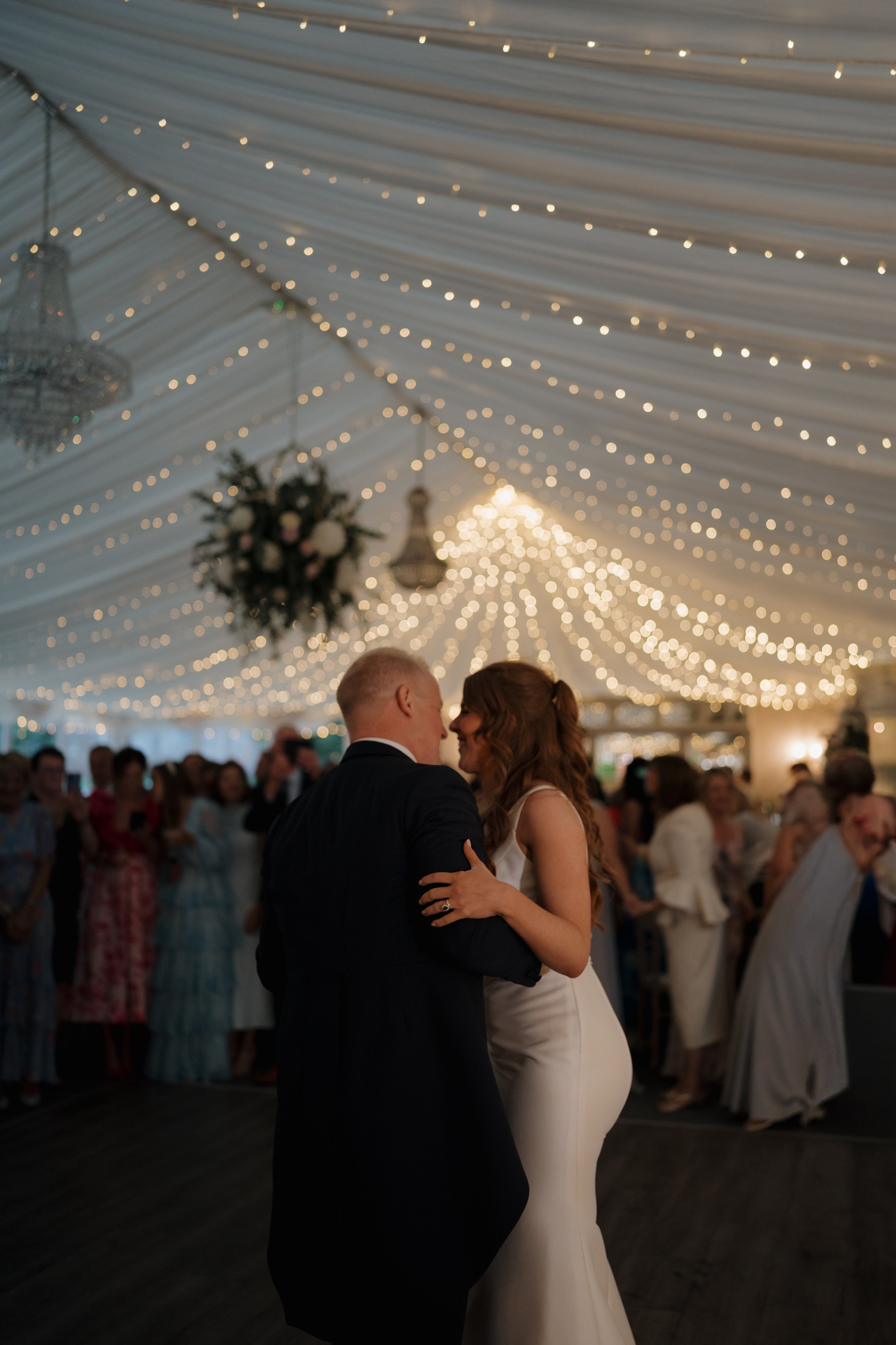 Couple sharing their first dance at a wedding reception in a decorated tent with string lights hanging from the ceiling in Ballyscullion Park.