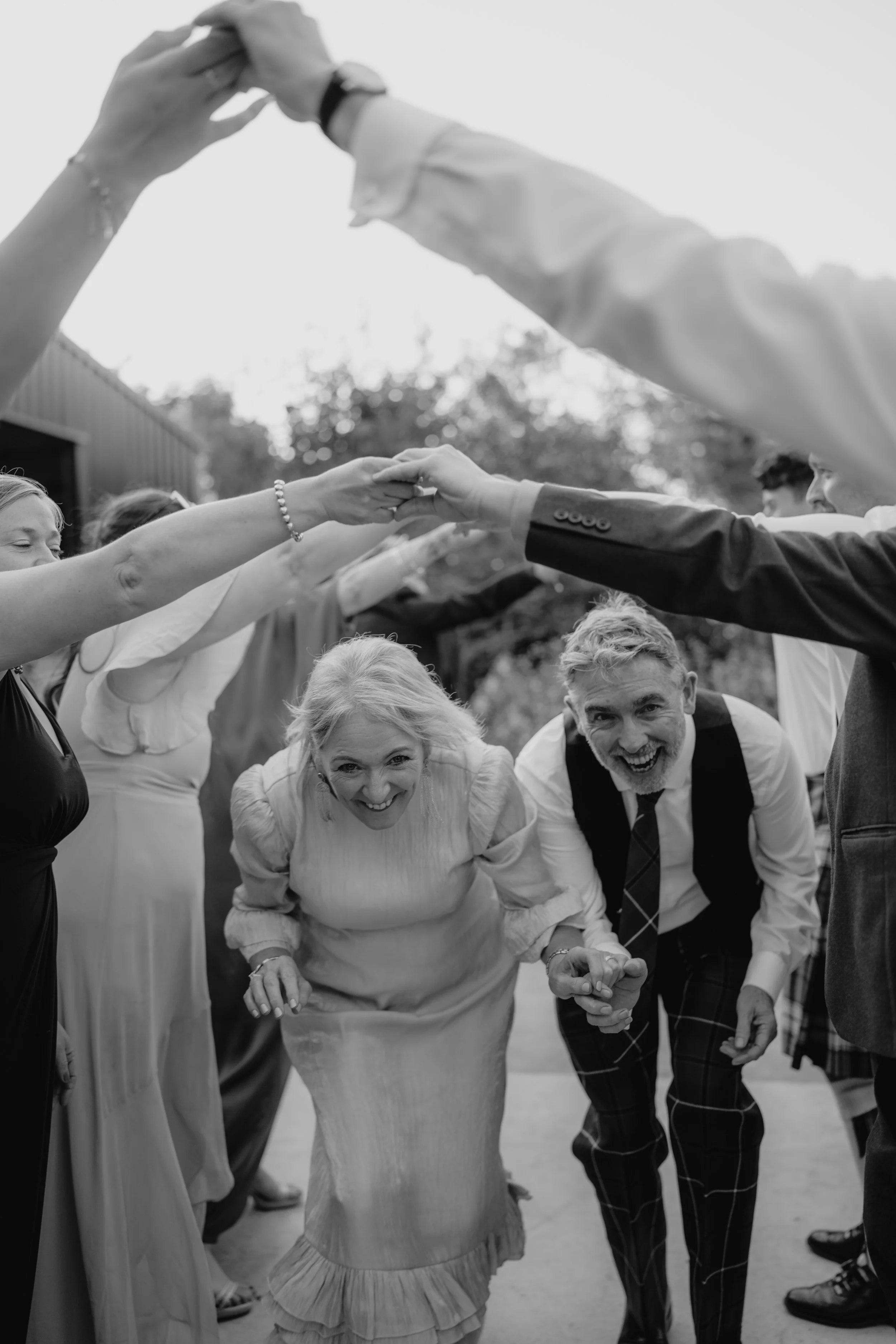 People celebrating outdoors, holding hands above, with smiling elderly woman and man in the center.
