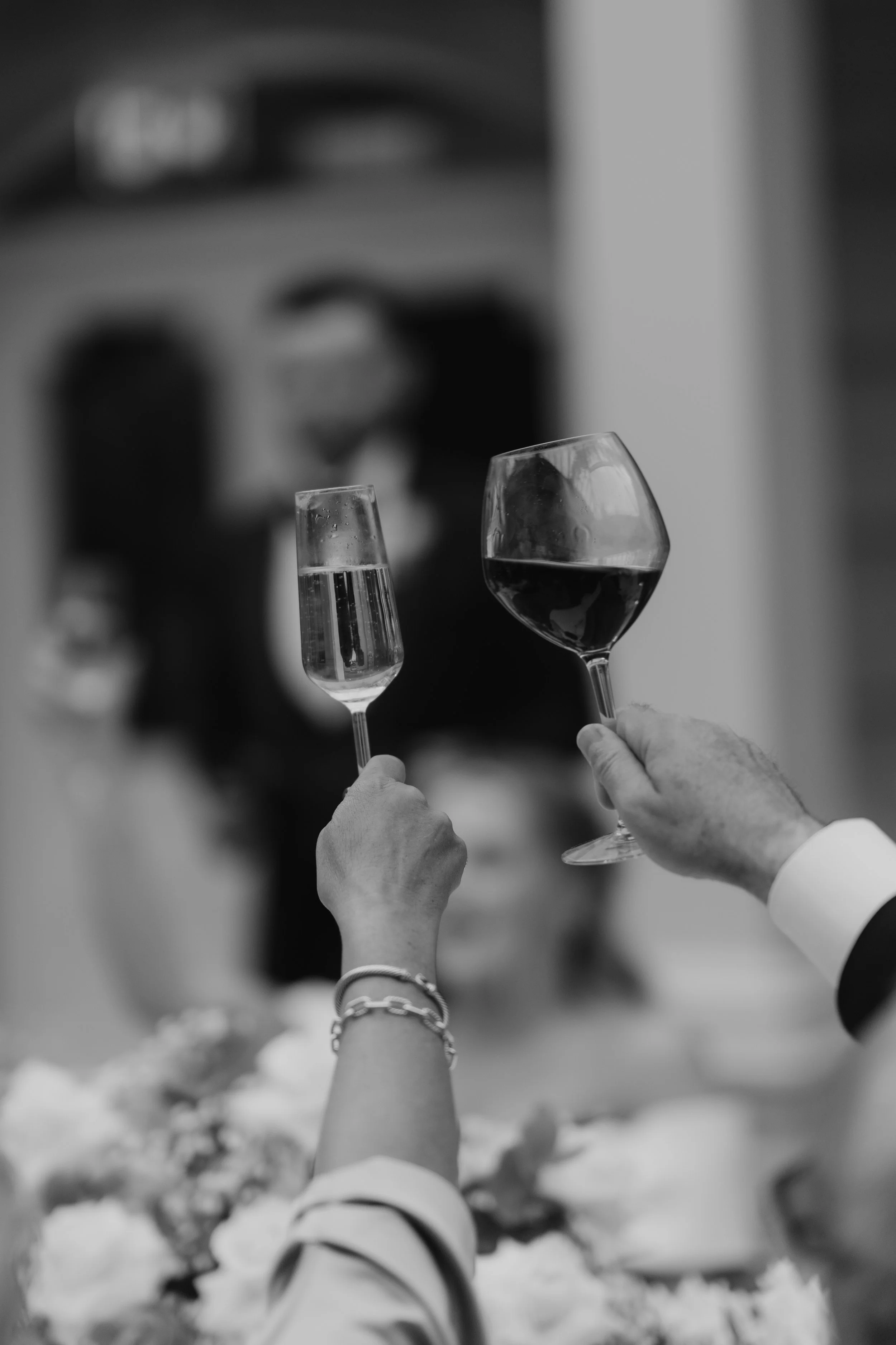 Two people toasting with glasses, one with champagne and the other with red wine, at an elegant celebration or dinner event.