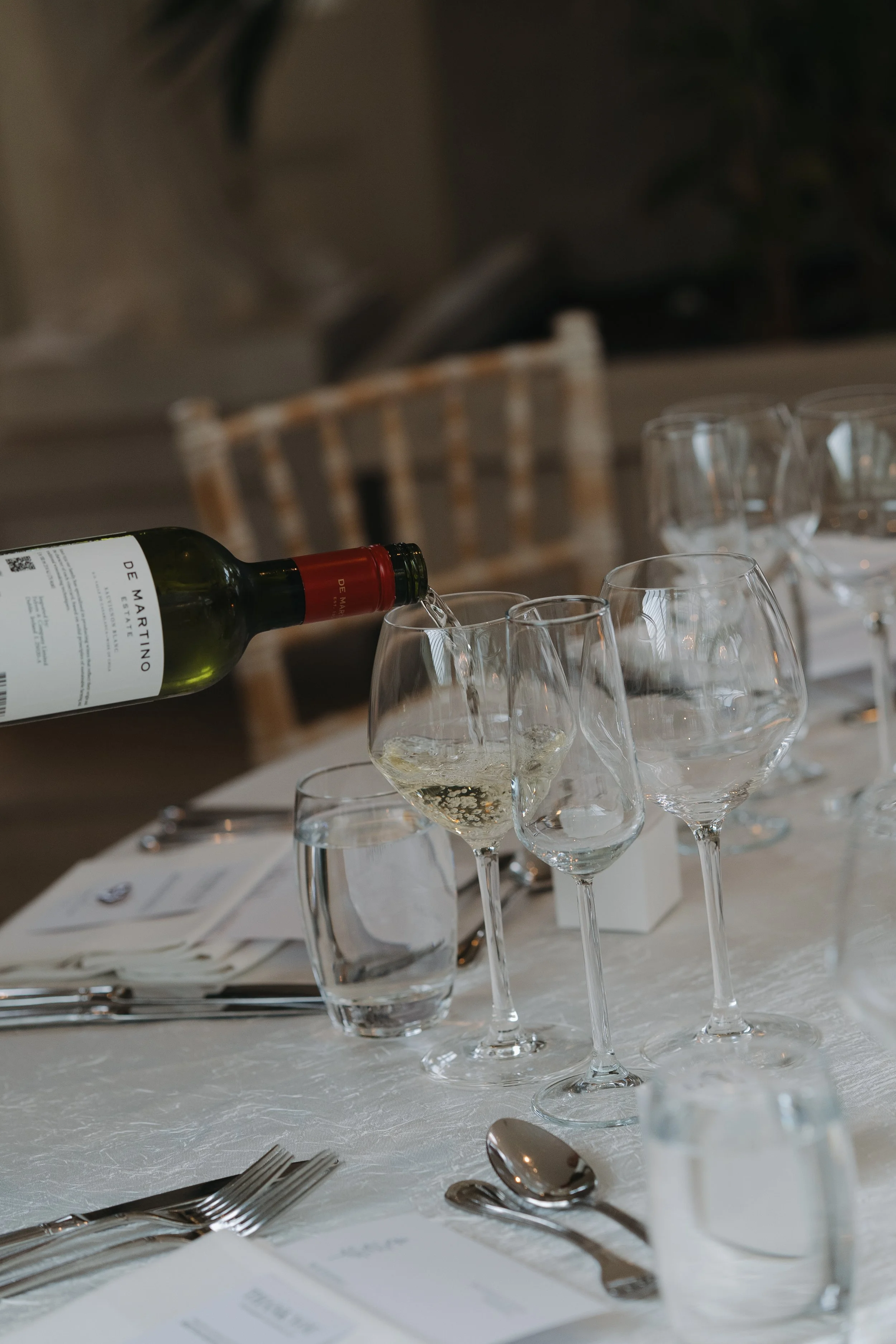 Wine glass being filled with white wine at a formal dining table.