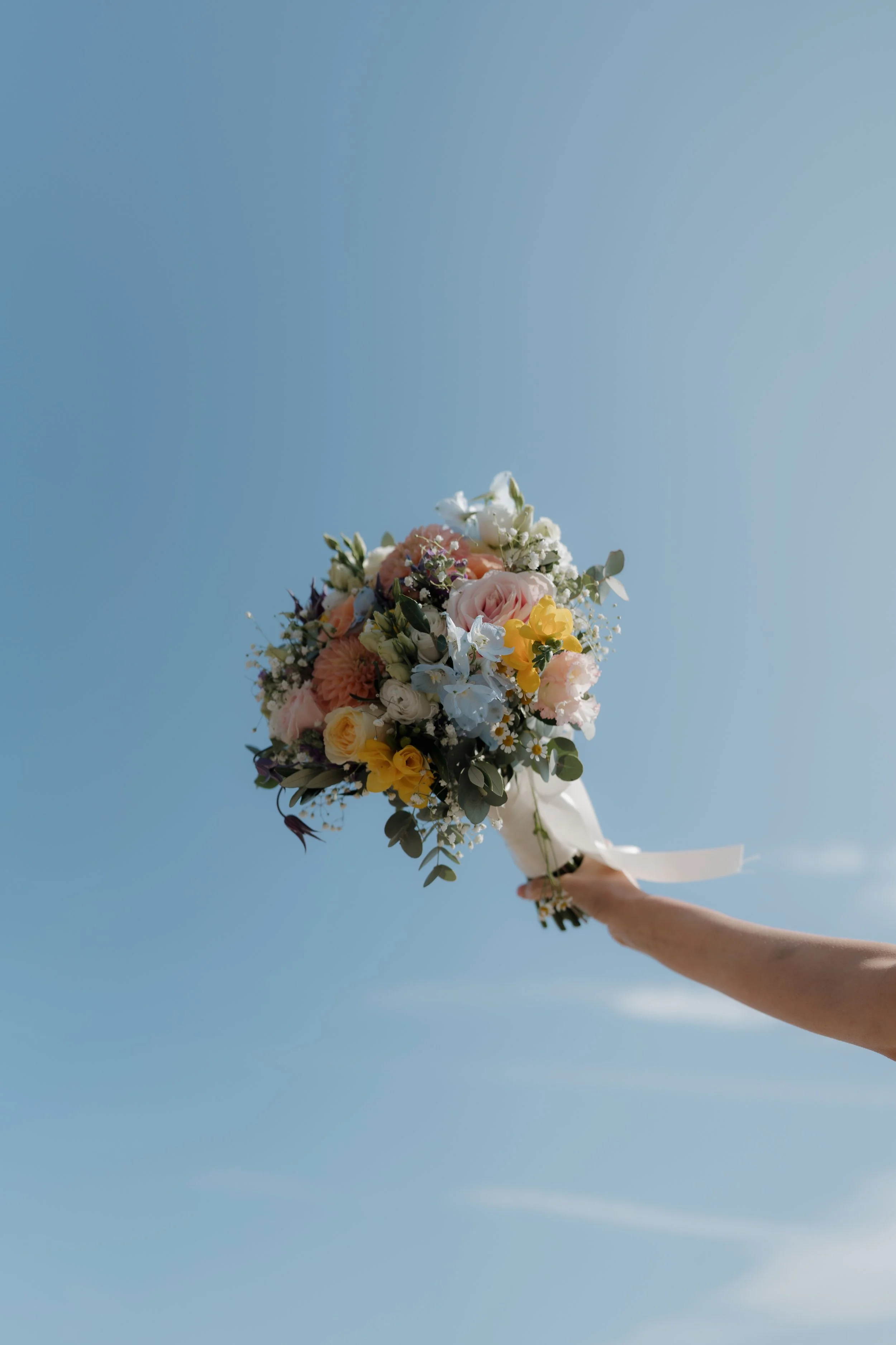 A person holding a bouquet of colorful flowers against a clear blue sky.