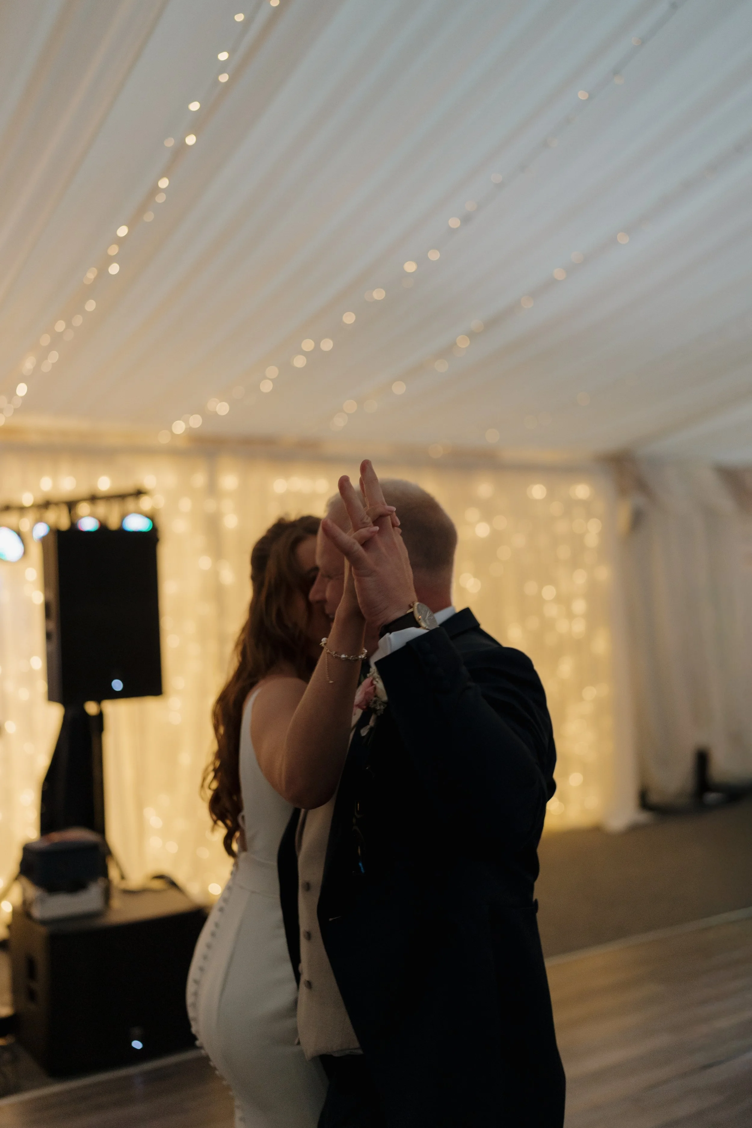 A bride and groom dance close together at their wedding reception under string lights and fairy lights.