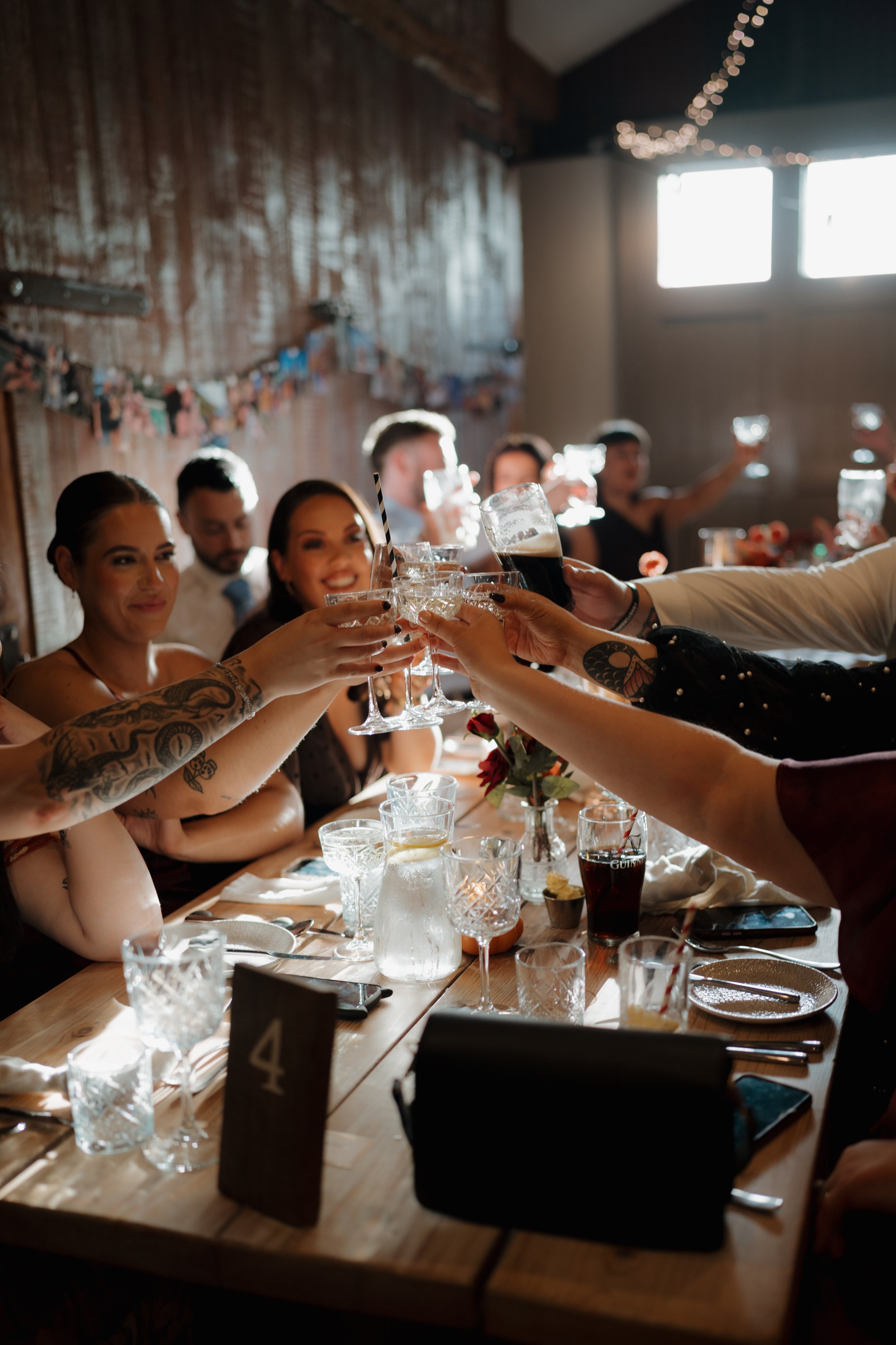 People raising glasses in a toast at a celebratory dinner gathering with bright natural light and festive decorations.