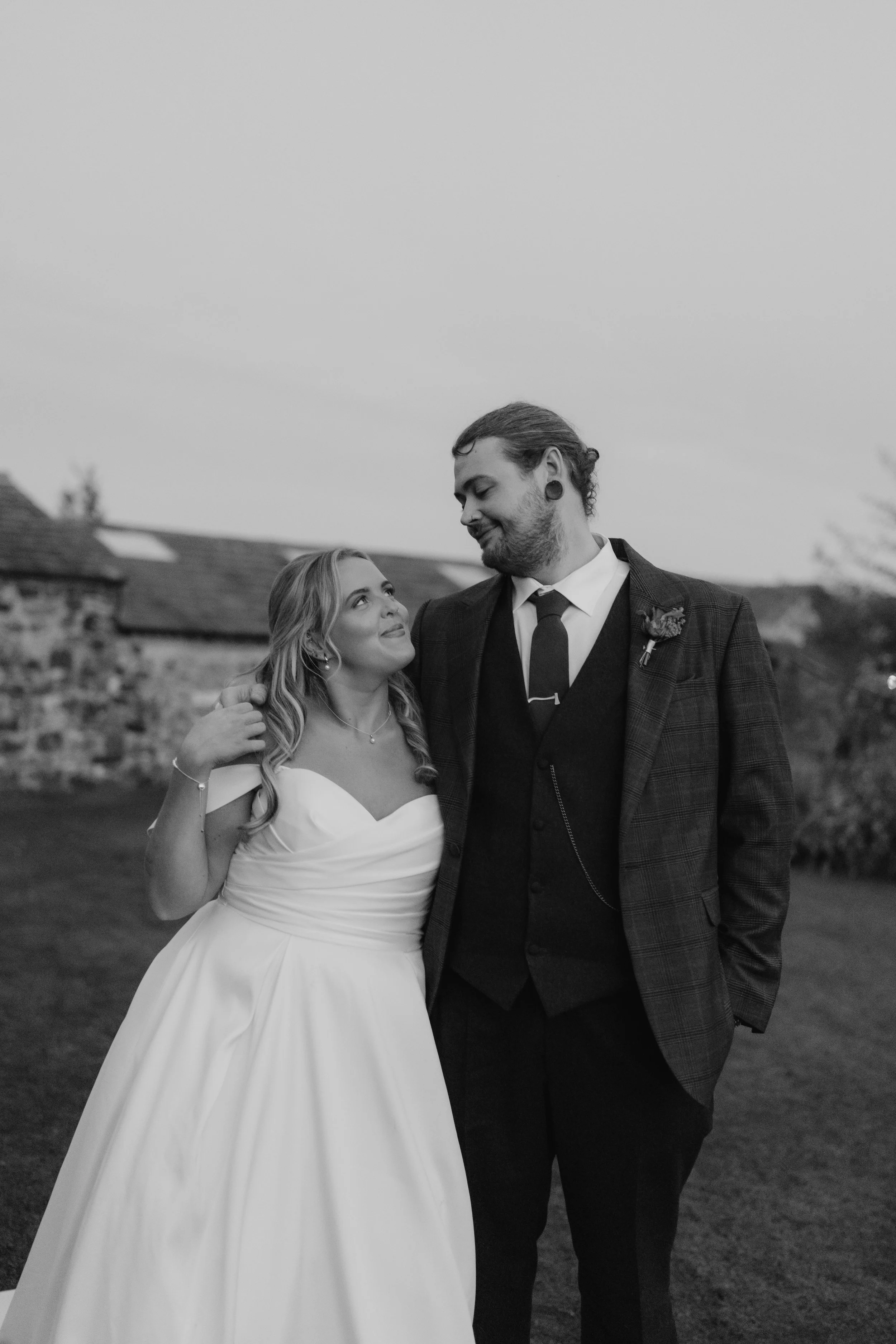 A bride and groom standing outdoors, looking at each other affectionately, on a cloudy day at Limepark.