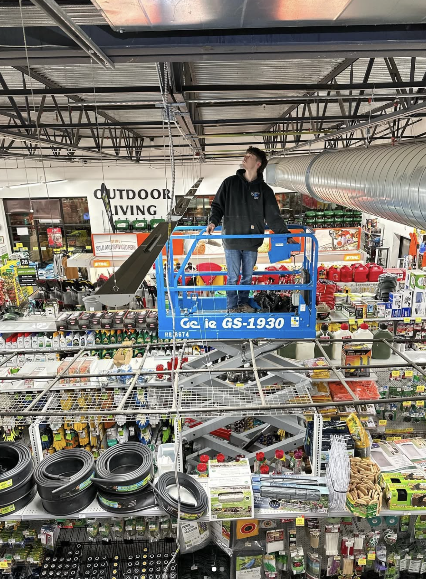 A person standing on a blue lift inside a hardware store, looking up at the ceiling.