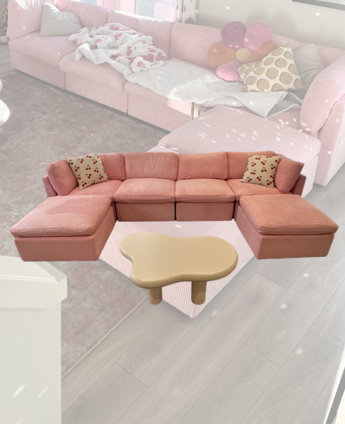 A pink sectional sofa with patterned pillows and a small cream-colored coffee table in a living room with light-colored hardwood floors and a gray carpet.
