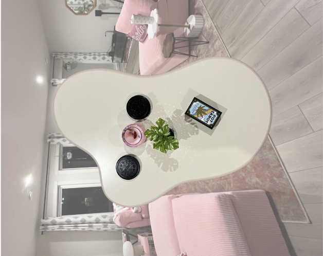 Decorative round mirror reflecting a room with pink furniture and plants, and a tablet displaying a tropical image.