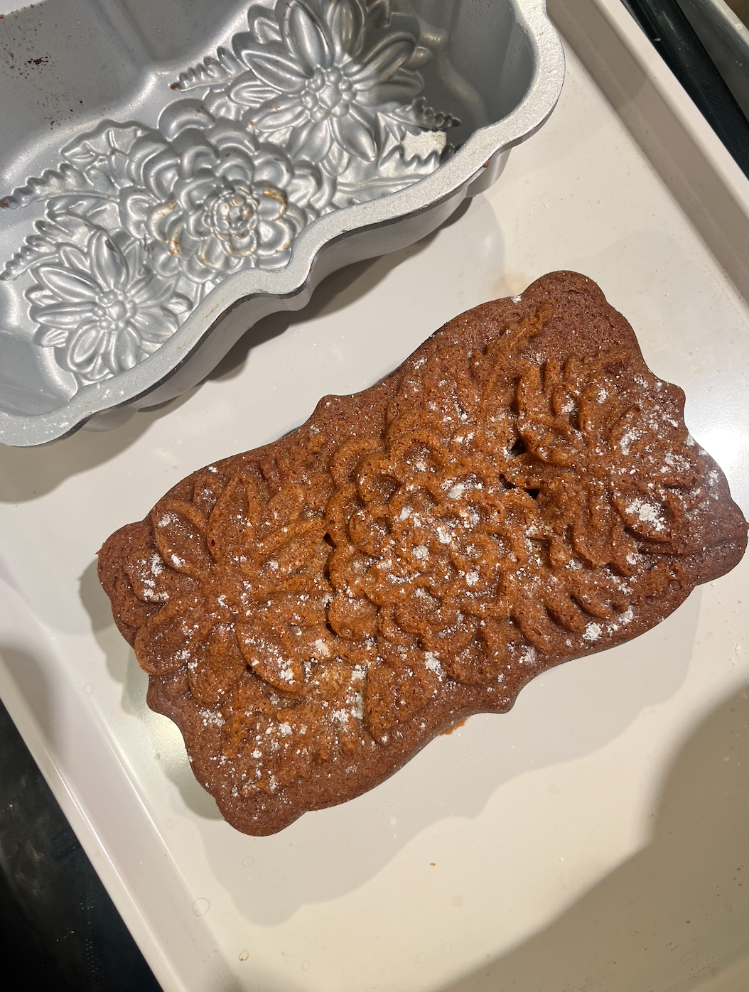 Decorated gingerbread cookie with floral designs and white powdered sugar, next to a metal cookie mold with floral patterns.