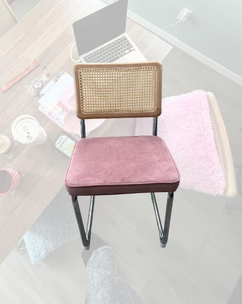 A pink cushioned chair with a caned backrest and black metal legs, seen from above on a wooden desk.