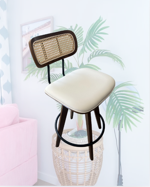 A barstool with a cushioned beige seat and woven rattan backrest is stacked on top of a woven basket in a bright room with tropical leaf wall art and a pink sofa.