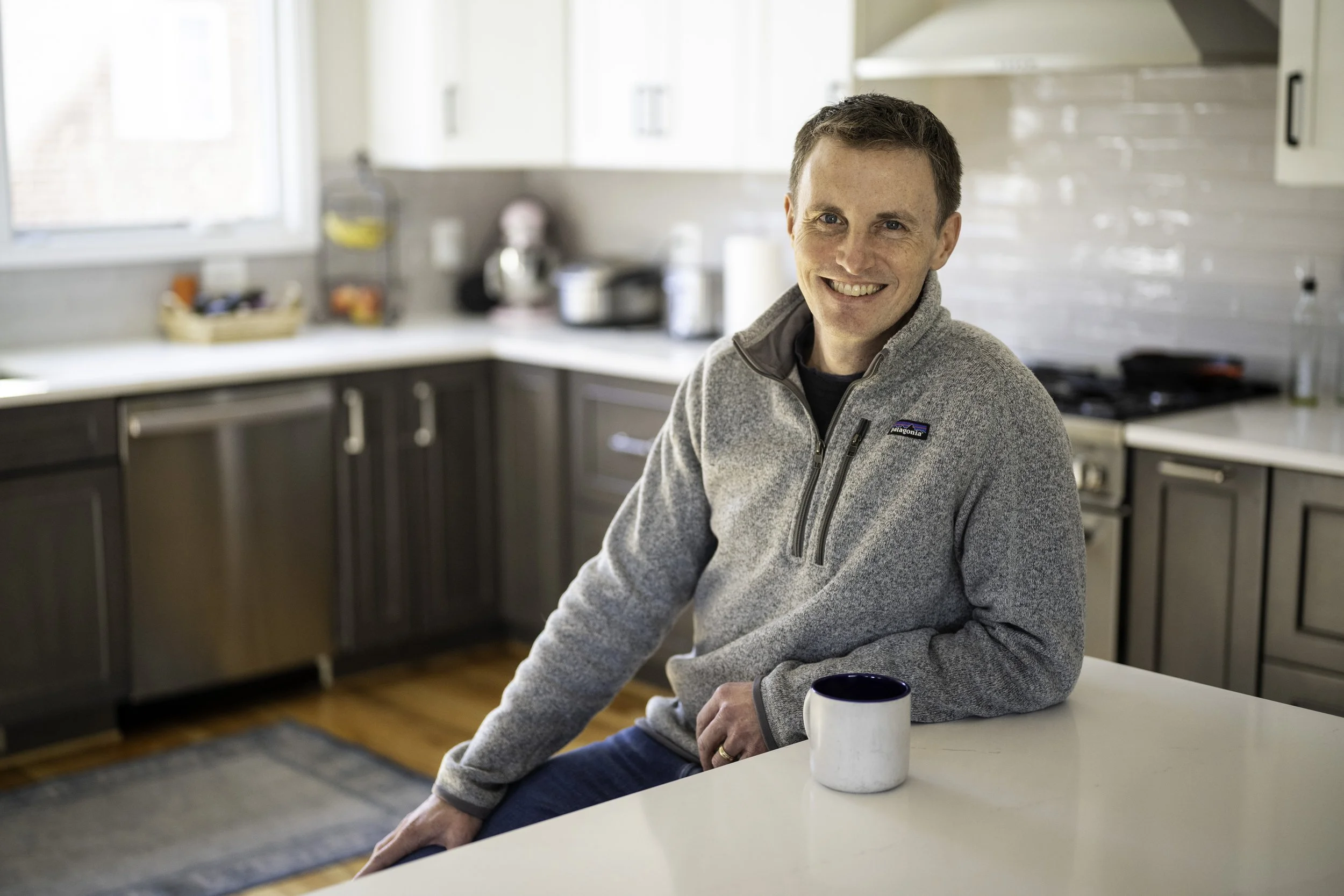 J.P. sitting at a kitchen island with a coffee mug, smiling at the camera.