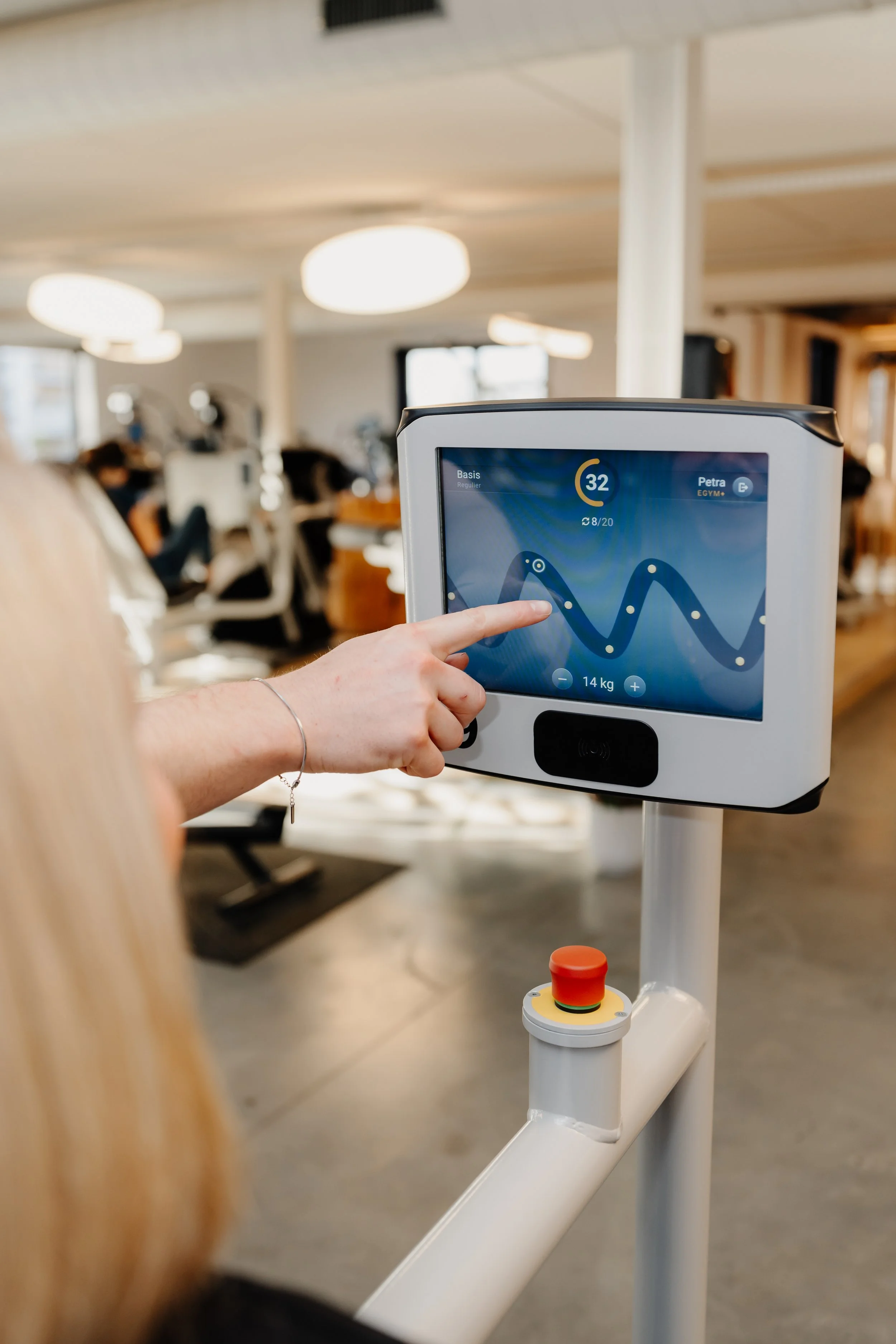 Een persoon wijst naar een touchscreen van een sportapparaat in een sportschool, met zwaardersafstellingen en grafieken op het scherm.