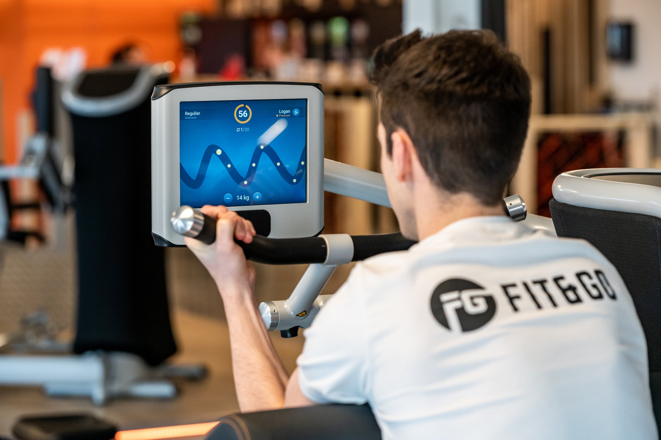 Een man zit op een loopband in een sportschool en houdt een handvat vast terwijl hij naar een scherm kijkt dat hartslag- en prestatiegegevens toont.