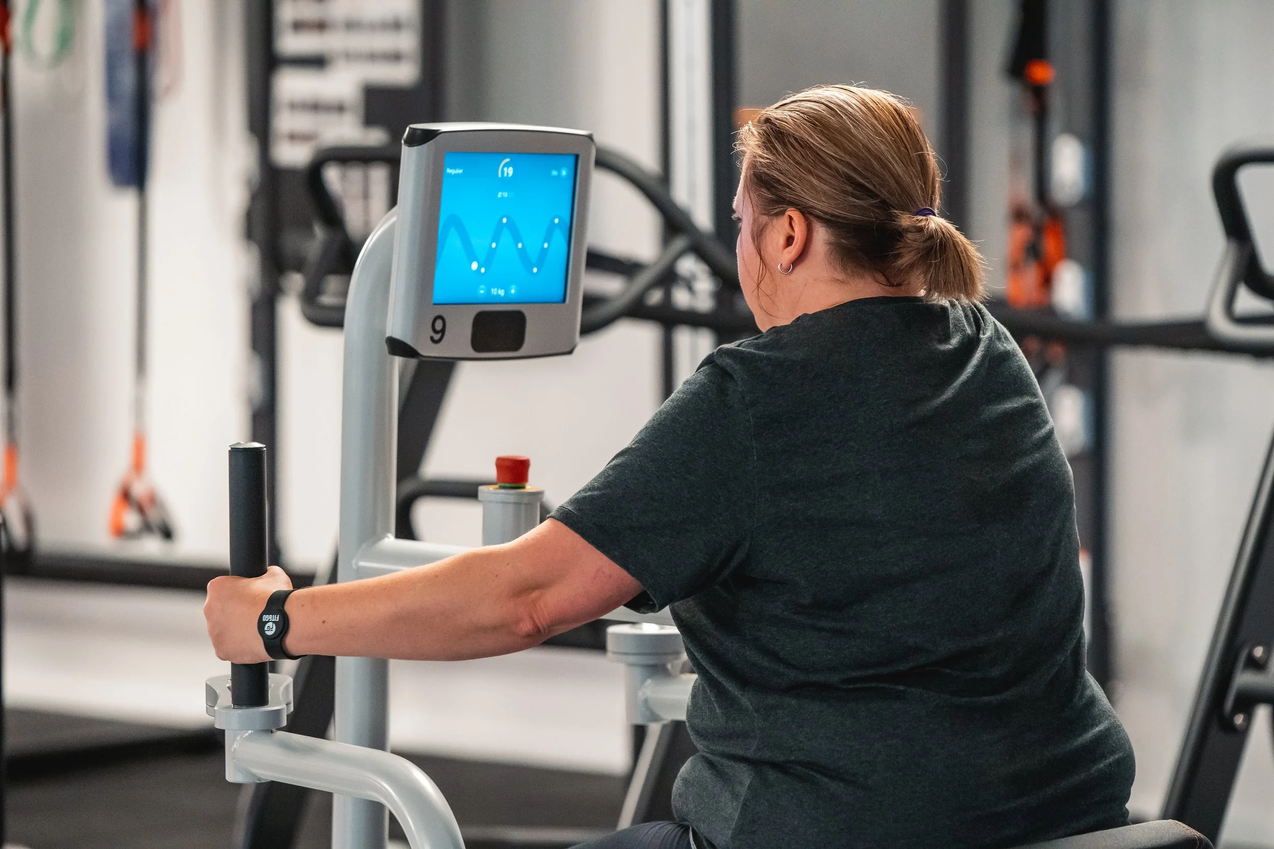 Vrouw die op een crosstrainer traint in een sportschool, met een scherm dat haar prestaties toont.