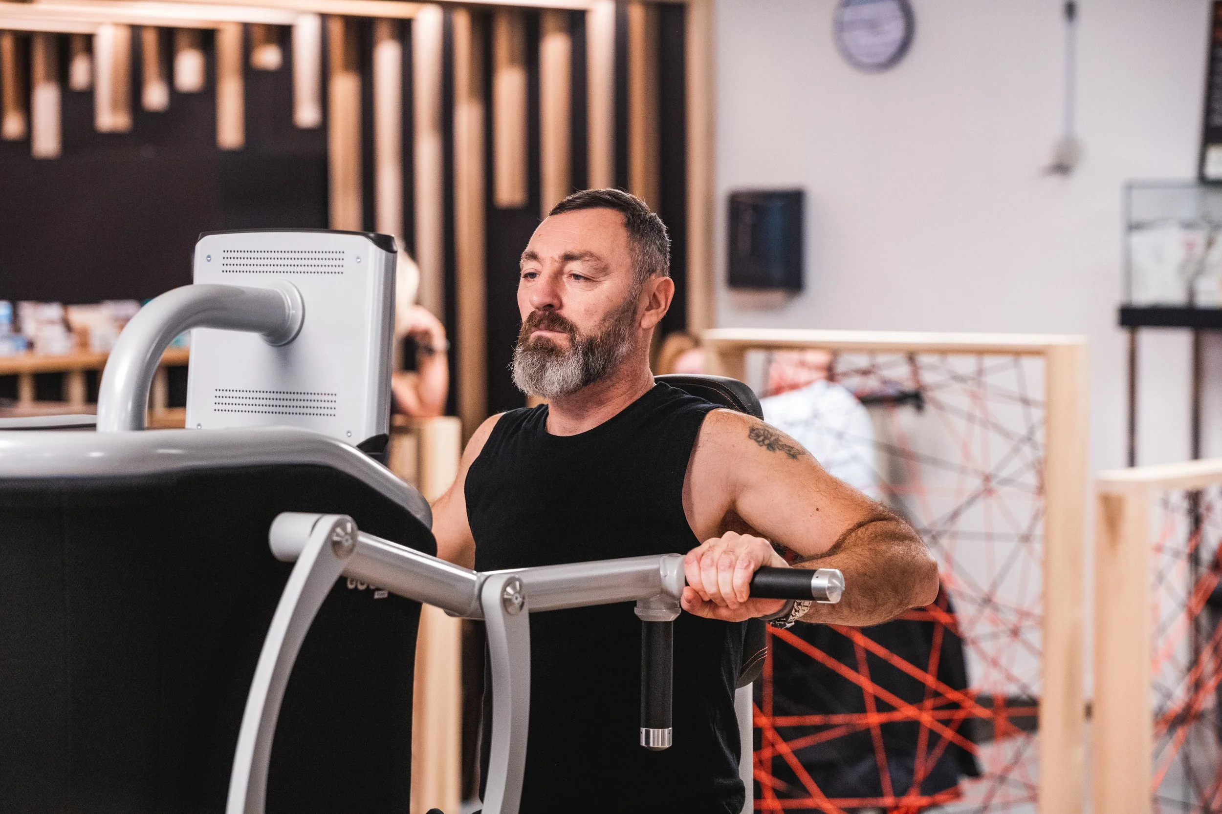 Man met een grijze baard op een loopband in een sportschool.