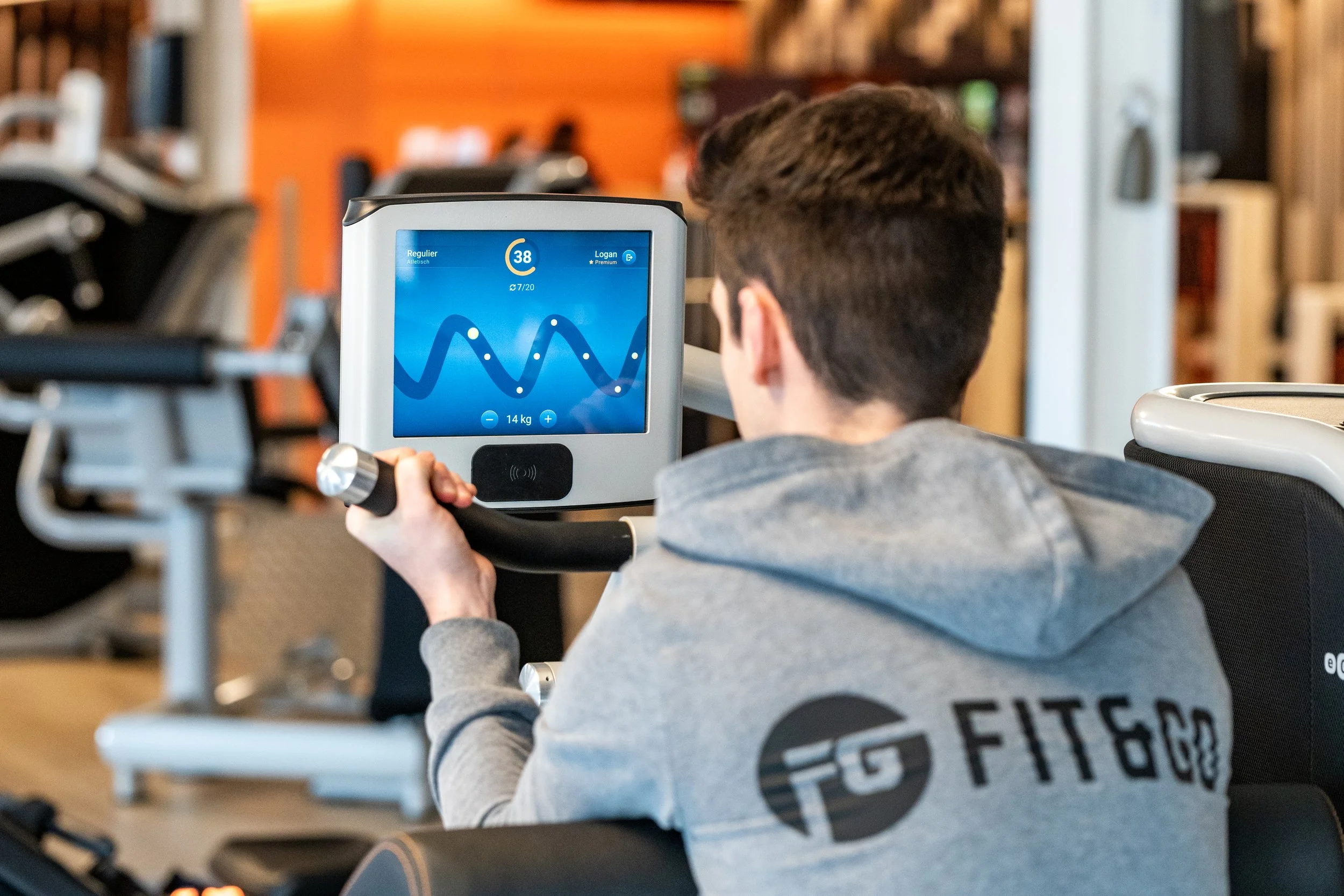 Een jonge man in een grijze hoodie die op een elliptische trainer traint in een sportschool.