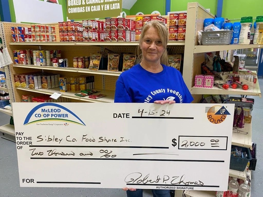 Woman Holding check for sibley county food share in front of canned goods