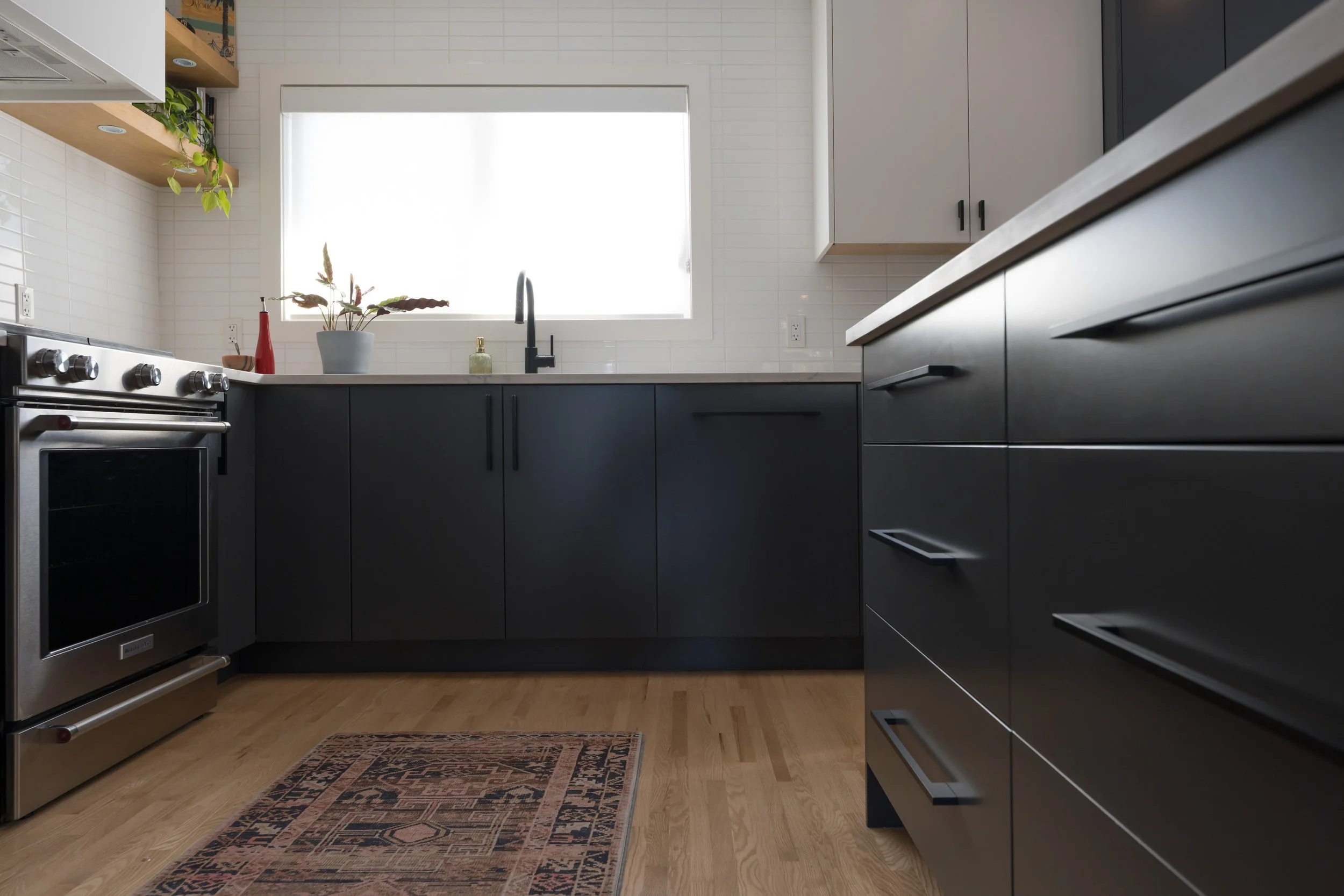 Sleek, contemporary kitchen design with dark cabinetry, white walls, and a large window above the sink. Bespoke kitchen cabinetry in a Calgary residence. 