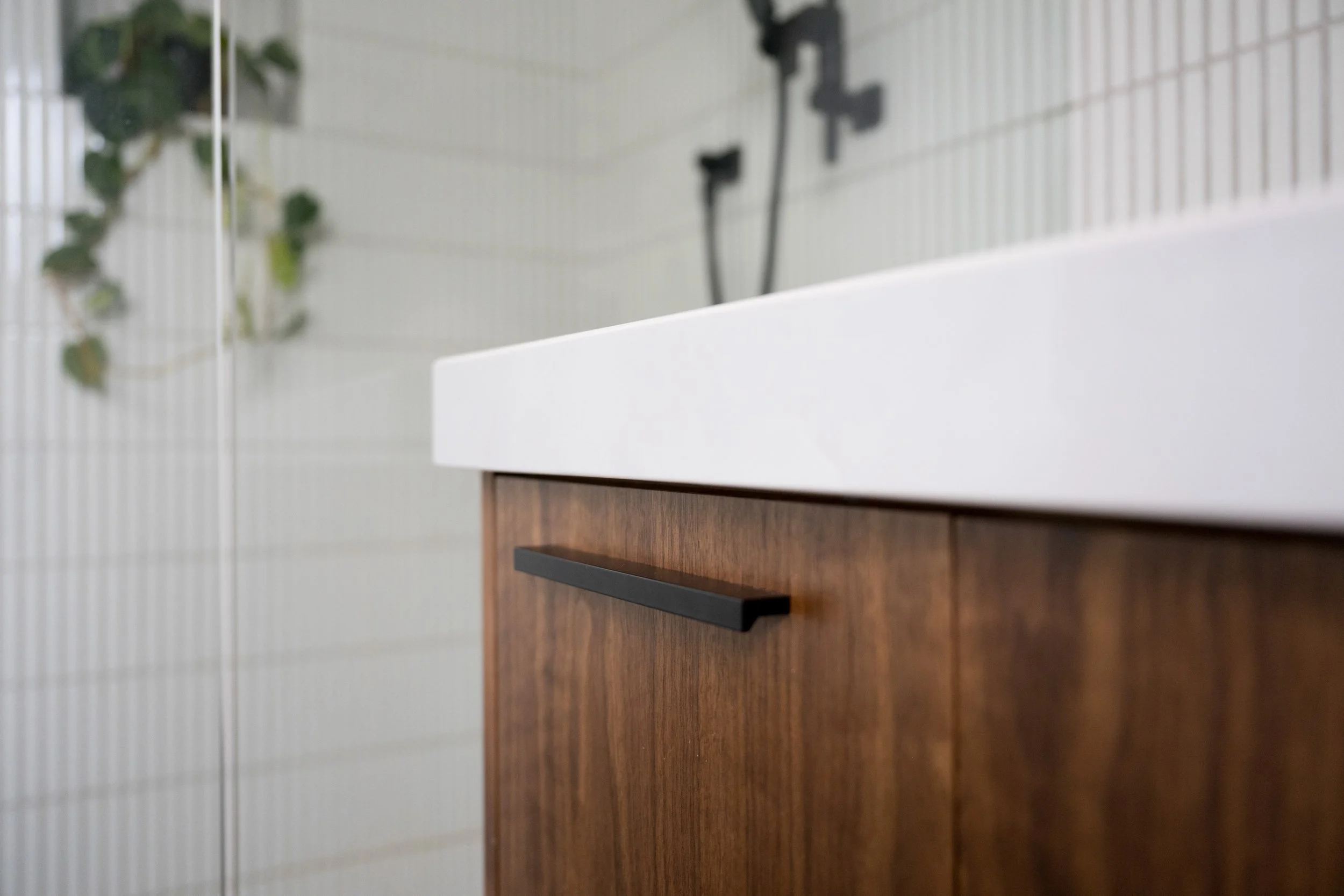 Close-up of a bathroom renovation featuring a wooden cabinet with a black handle, white countertop, and white tiled wall in the background.