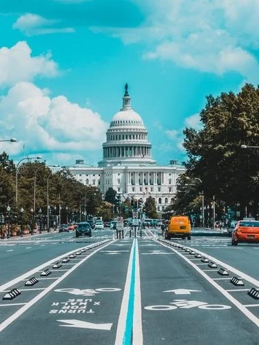 View of the U.S. Capitol building in Washington, D.C., from a street with bike lanes, cars, and trees on either side.