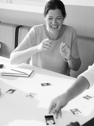 A woman laughing and playing a card game with another person at a table.