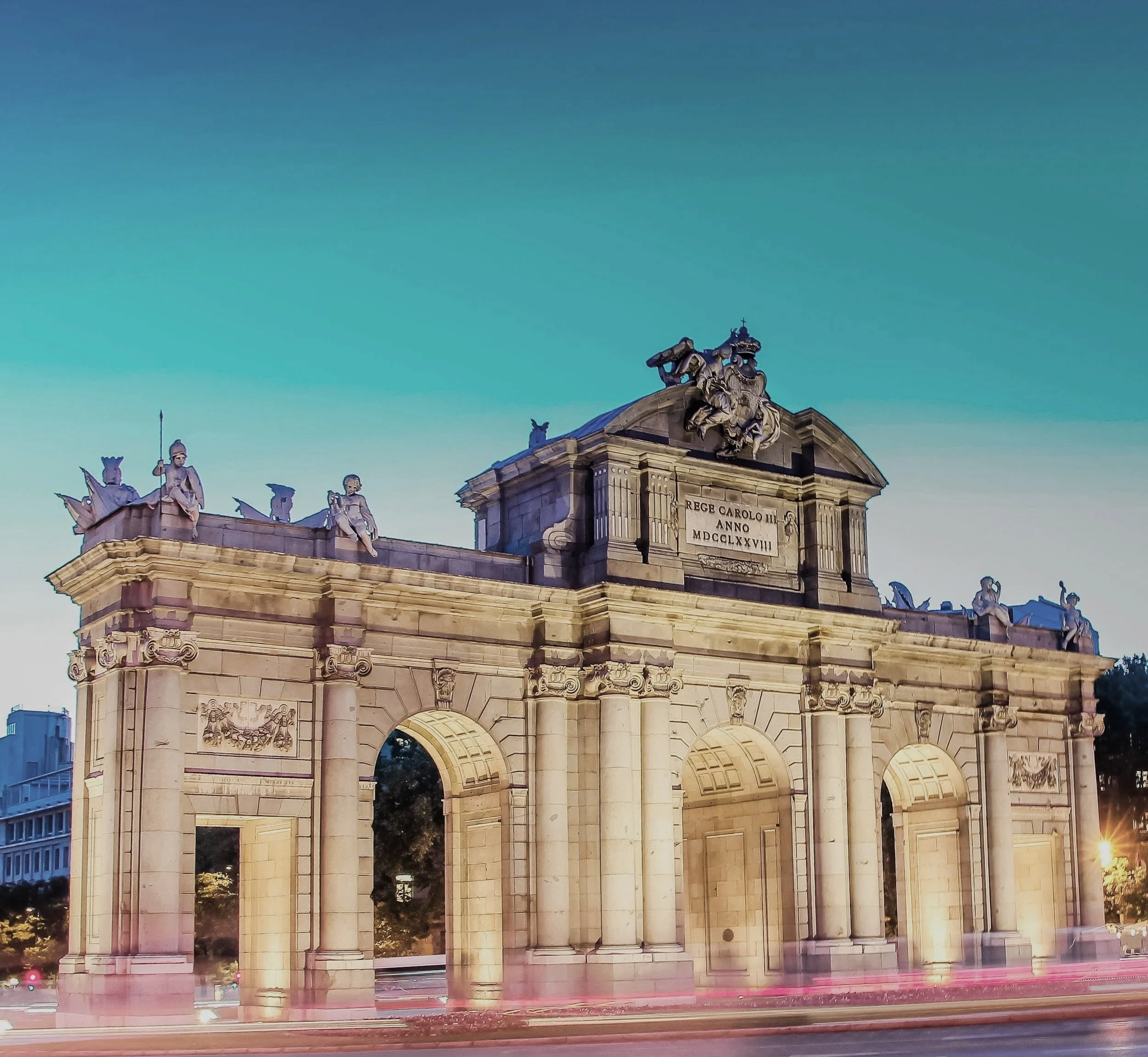 Arco de la Independencia en un atardecer con cielo azul, con esculturas y detalles arquitectónicos en piedra, en una ciudad.