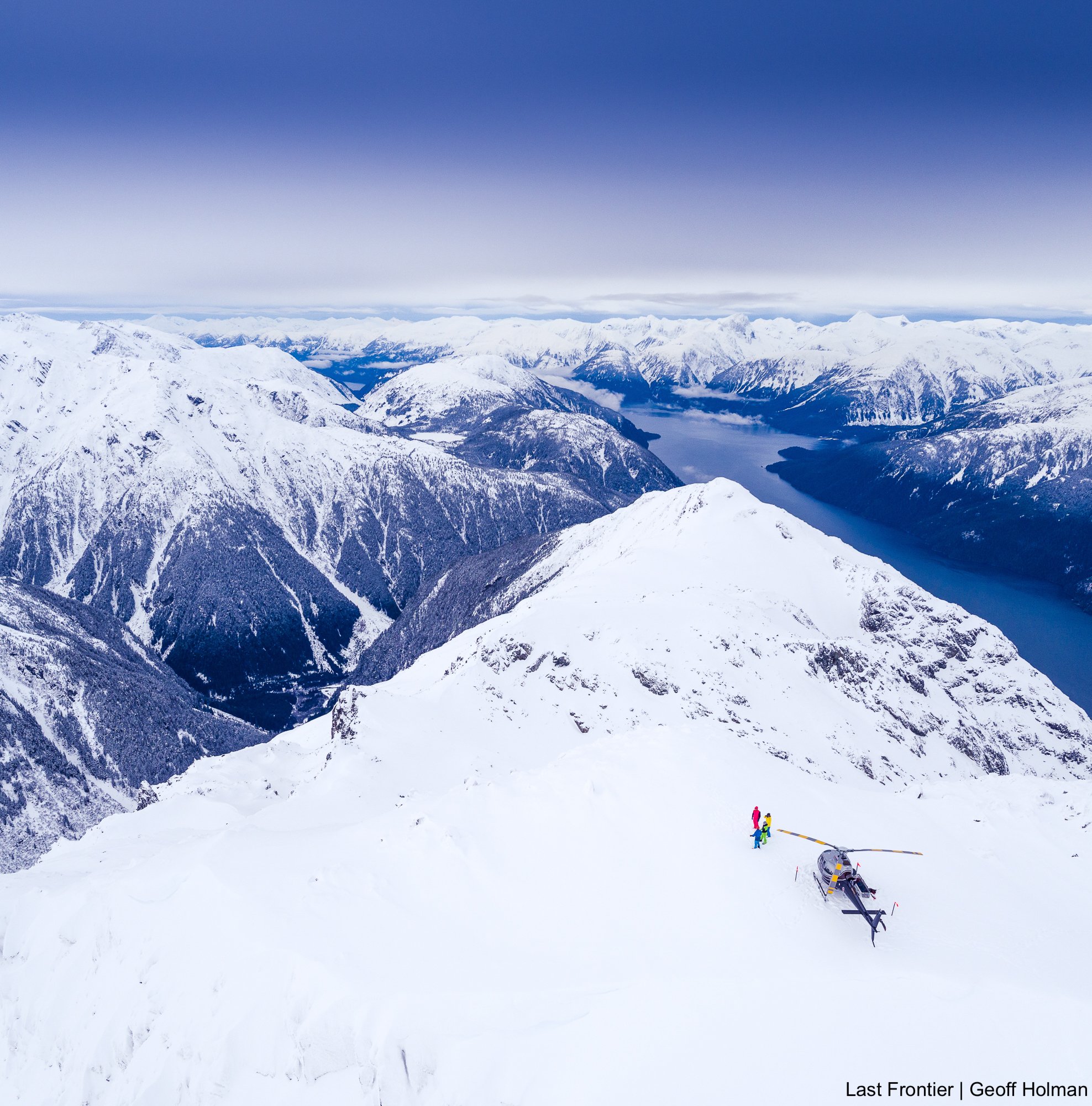 Skier standing beside the helicopter on a ridge overlooking the Portland Canal near Stewart, BC.
