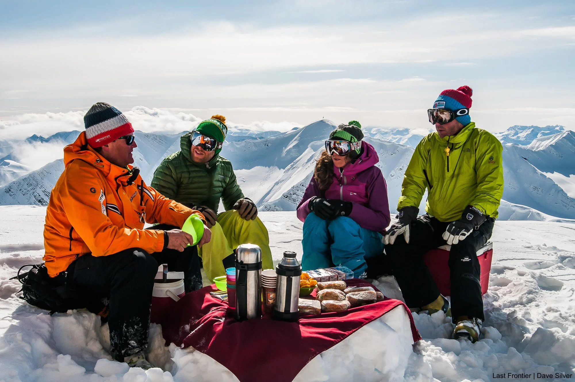 Guests enjoying a picnic lunch on a mountain ridge during a day of heli skiing at Bell 2.