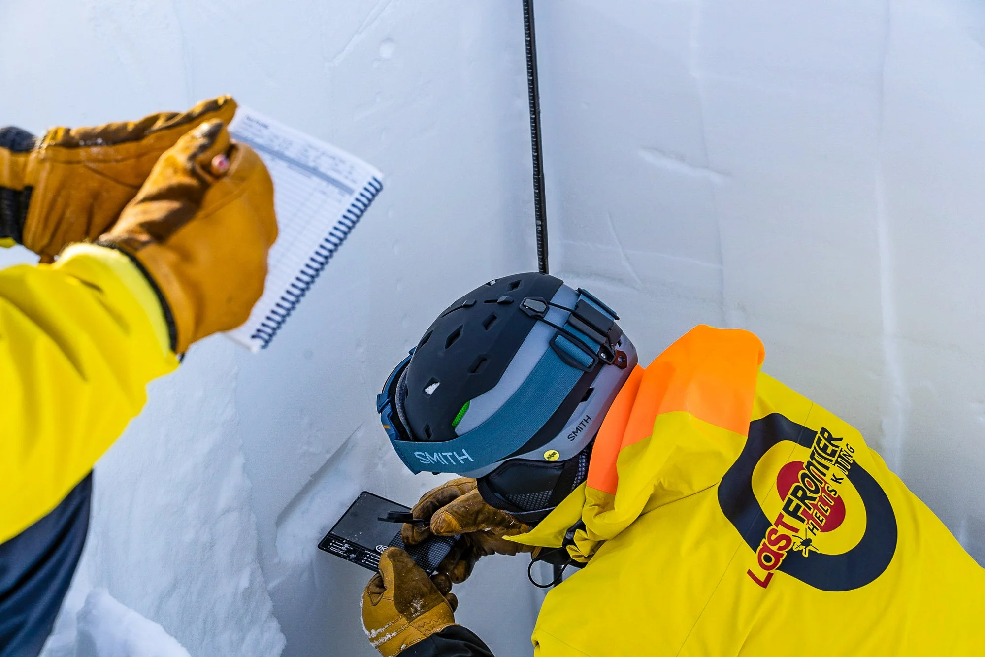 Last Frontier Heliskiing guide performing a snow pit assessment, analyzing snow crystals and layers to evaluate snowpack conditions in British Columbia’s backcountry