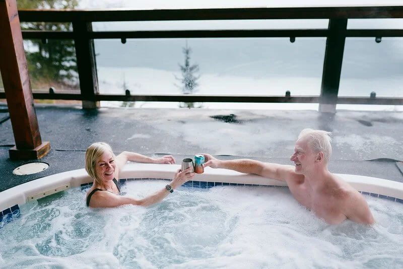 Guests enjoying a beer in the outdoor hot tub overlooking Quesnel Lake after skiing.