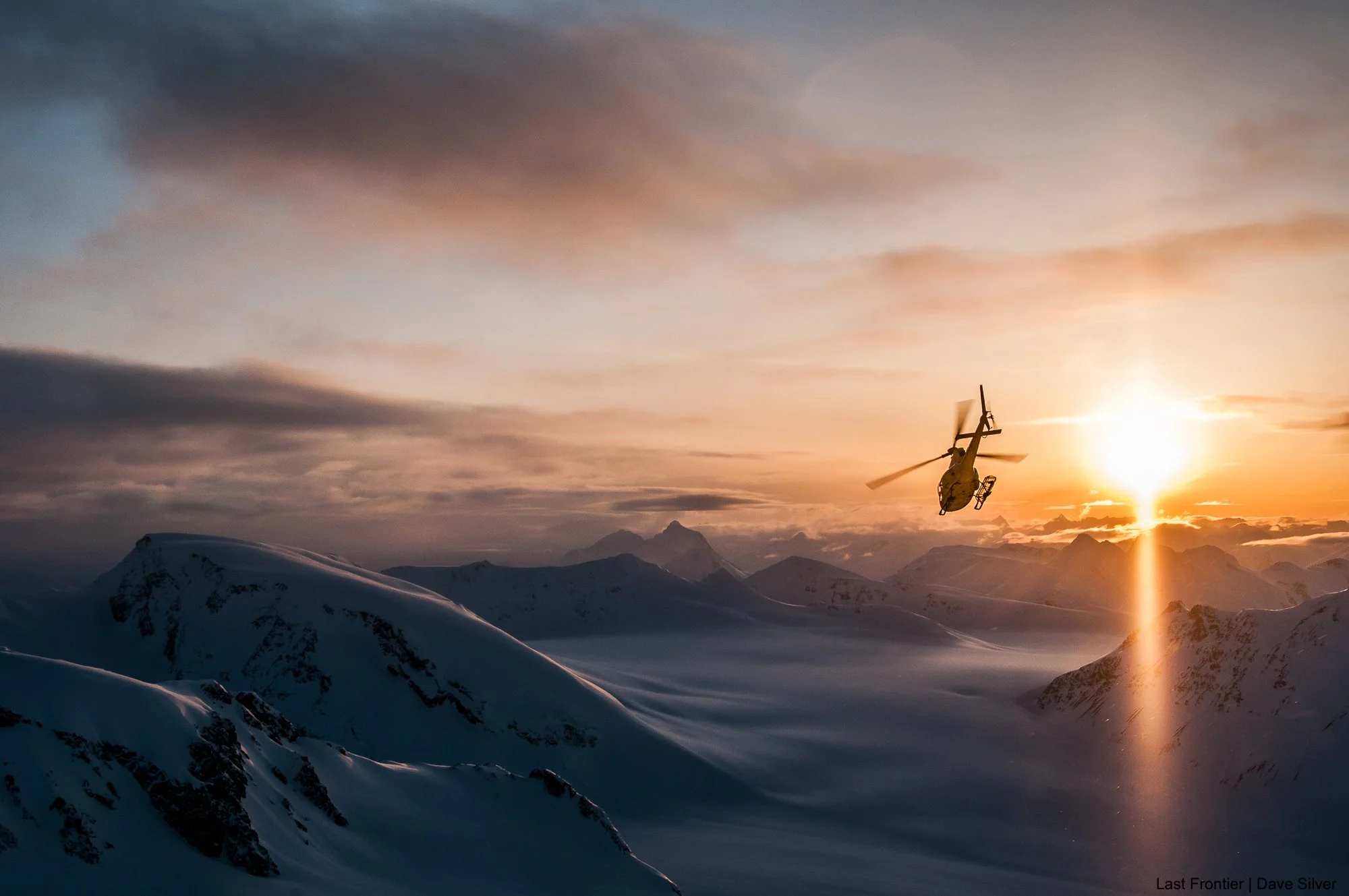 Last Frontier helicopter flying through the mountains at sunset near Ripley Creek.