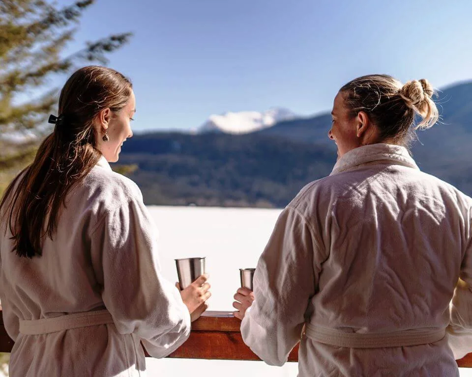 Guests relaxing with drinks overlooking frozen Quesnel Lake after a day of skiing