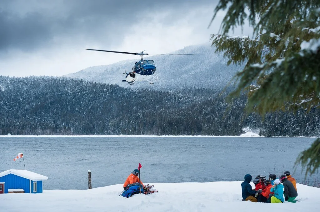 Skiers preparing for a helicopter pickup beside frozen Quesnel Lake.