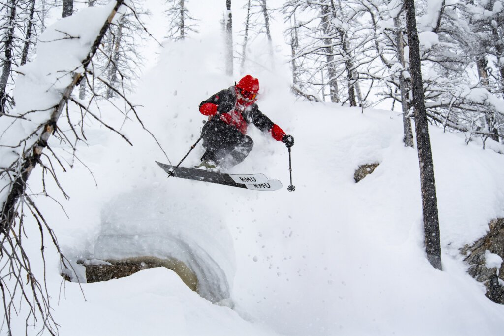 Heli-skier launches off a powder-covered pillow in a burn at Silvertip